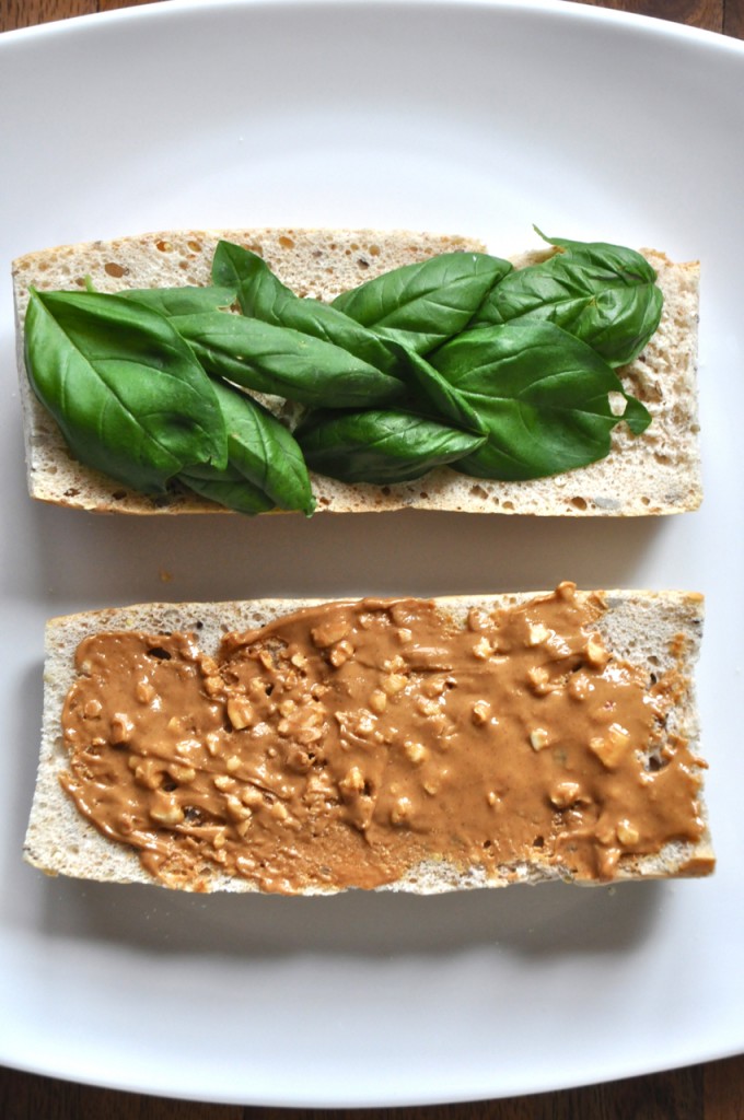 Plate with two slices of bread topped with basil on one and peanut butter on the other