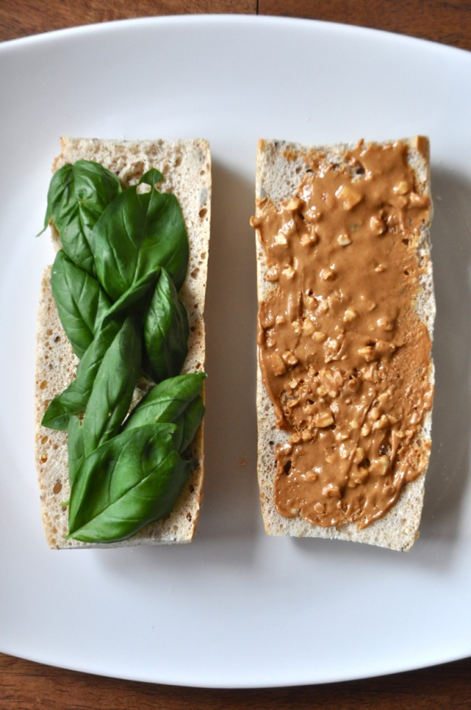 Slices of bread topped with fresh basil and peanut butter for making a healthy vegan sandwich