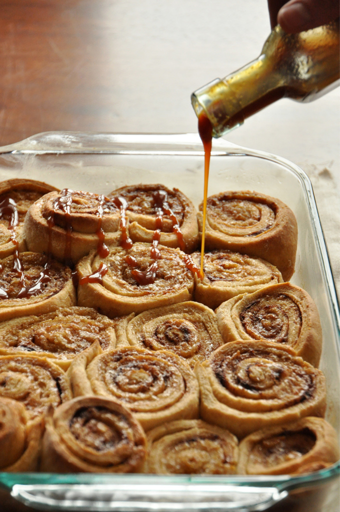 Pouring caramel sauce over a batch of our Overnight Honey Wheat Cinnamon Rolls recipe