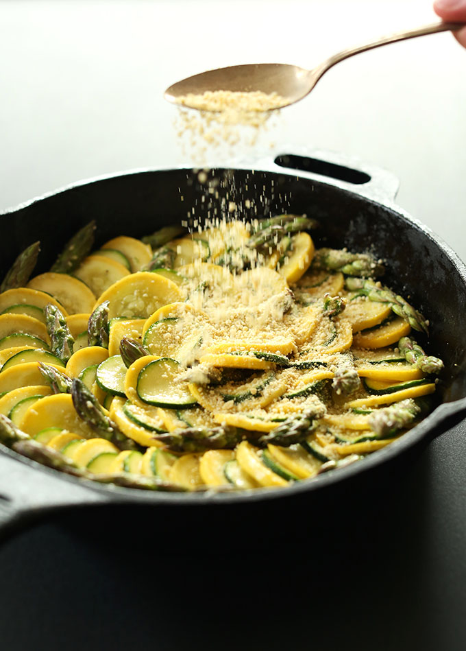 Sprinkling vegan parmesan over Zucchini Asparagus Gratin