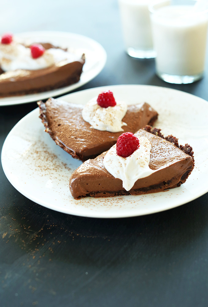 Slices of Vegan Chocolate Silk Pie topped with coconut whipped cream and fresh raspberries