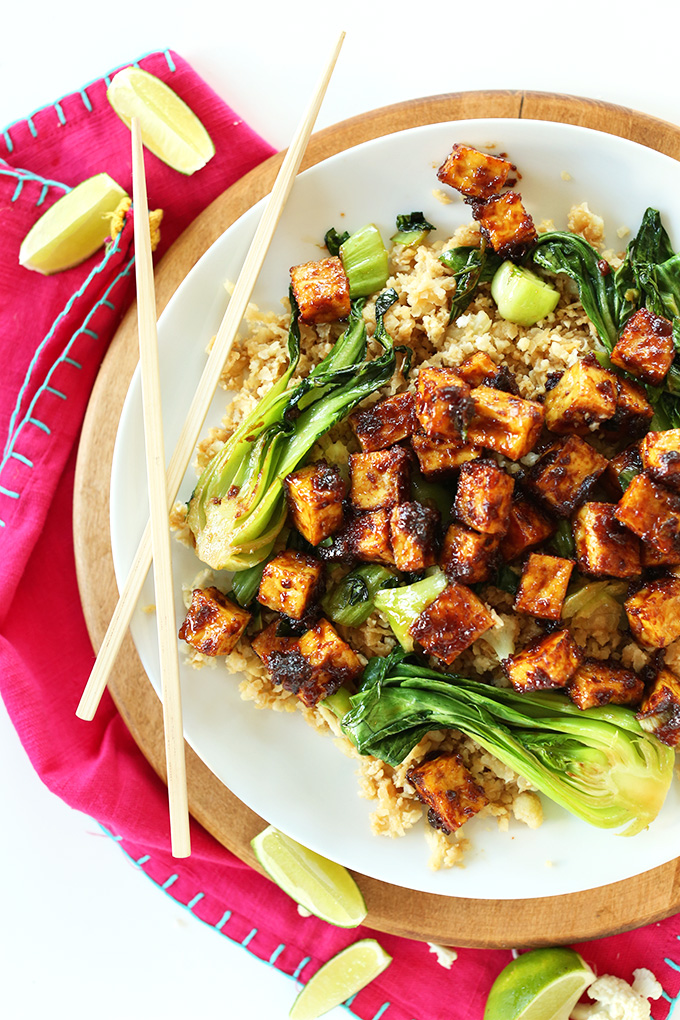 Chopsticks resting on a plate of cauliflower rice, bok choy, and Easy Crispy Tofu with Peanut Glaze