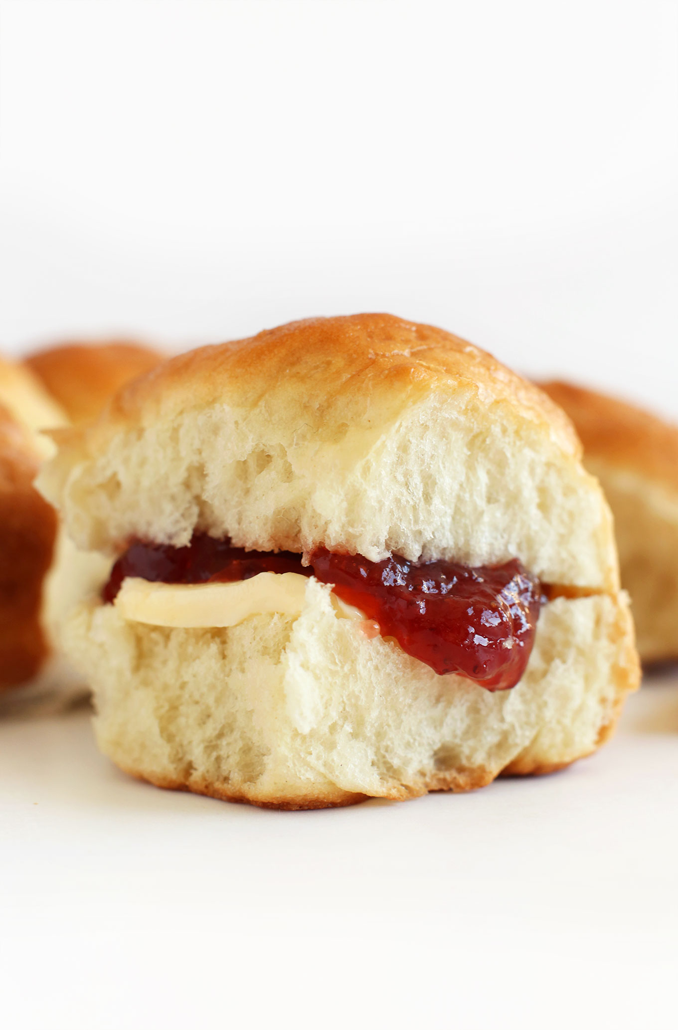 Close up shot of a soft and buttery vegan dinner roll with jam and vegan butter