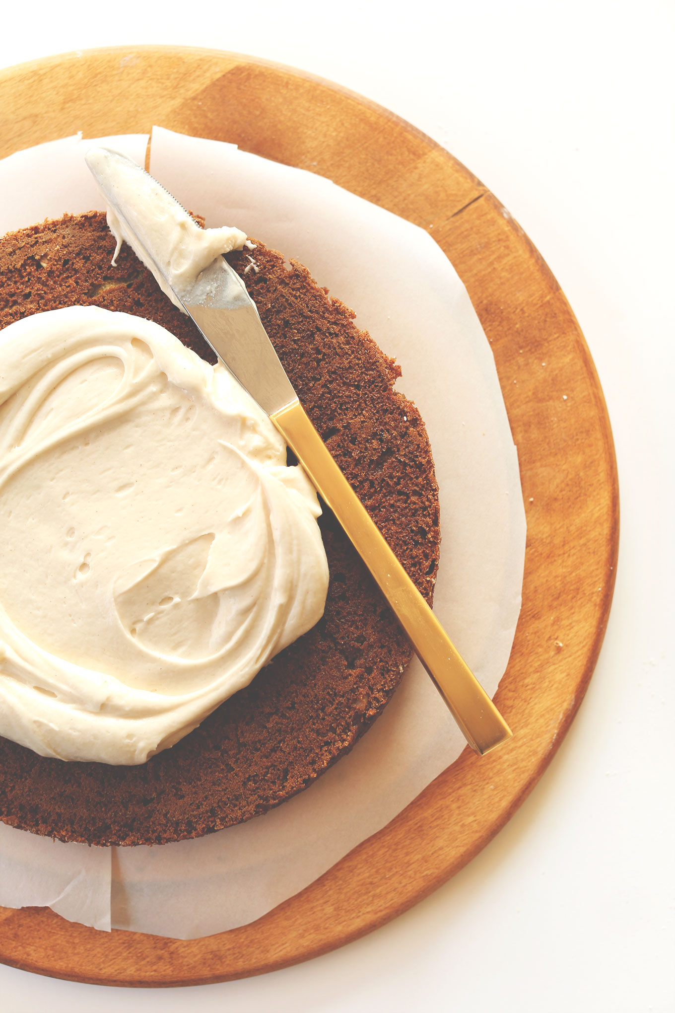 Using a butter knife to spread Vegan Cream Cheese Frosting onto a cake