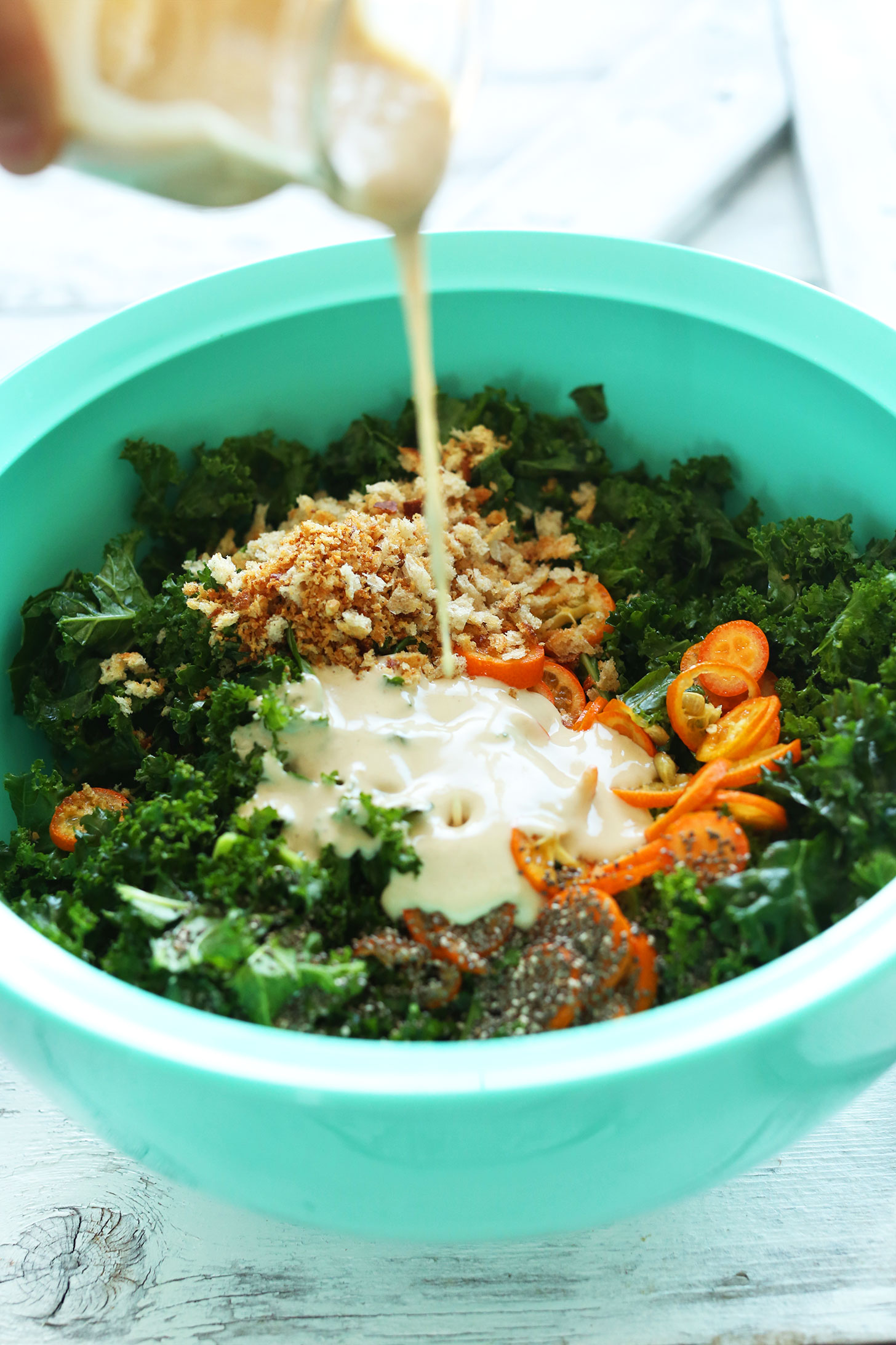 Pouring tahini dressing onto a satisfying vegan kale salad recipe
