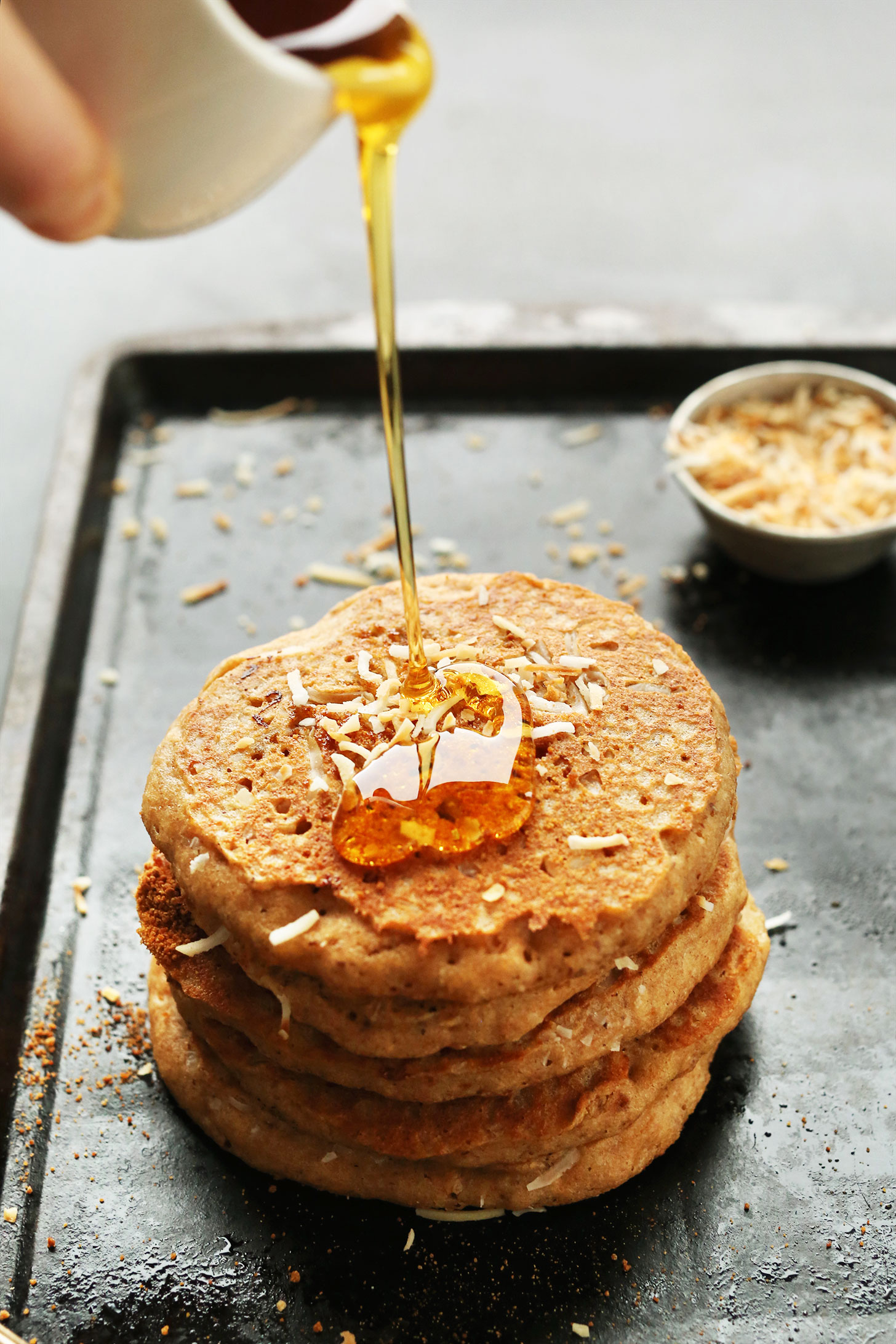 Pouring maple syrup onto a stack of delicious Vegan Toasted Coconut Pancakes