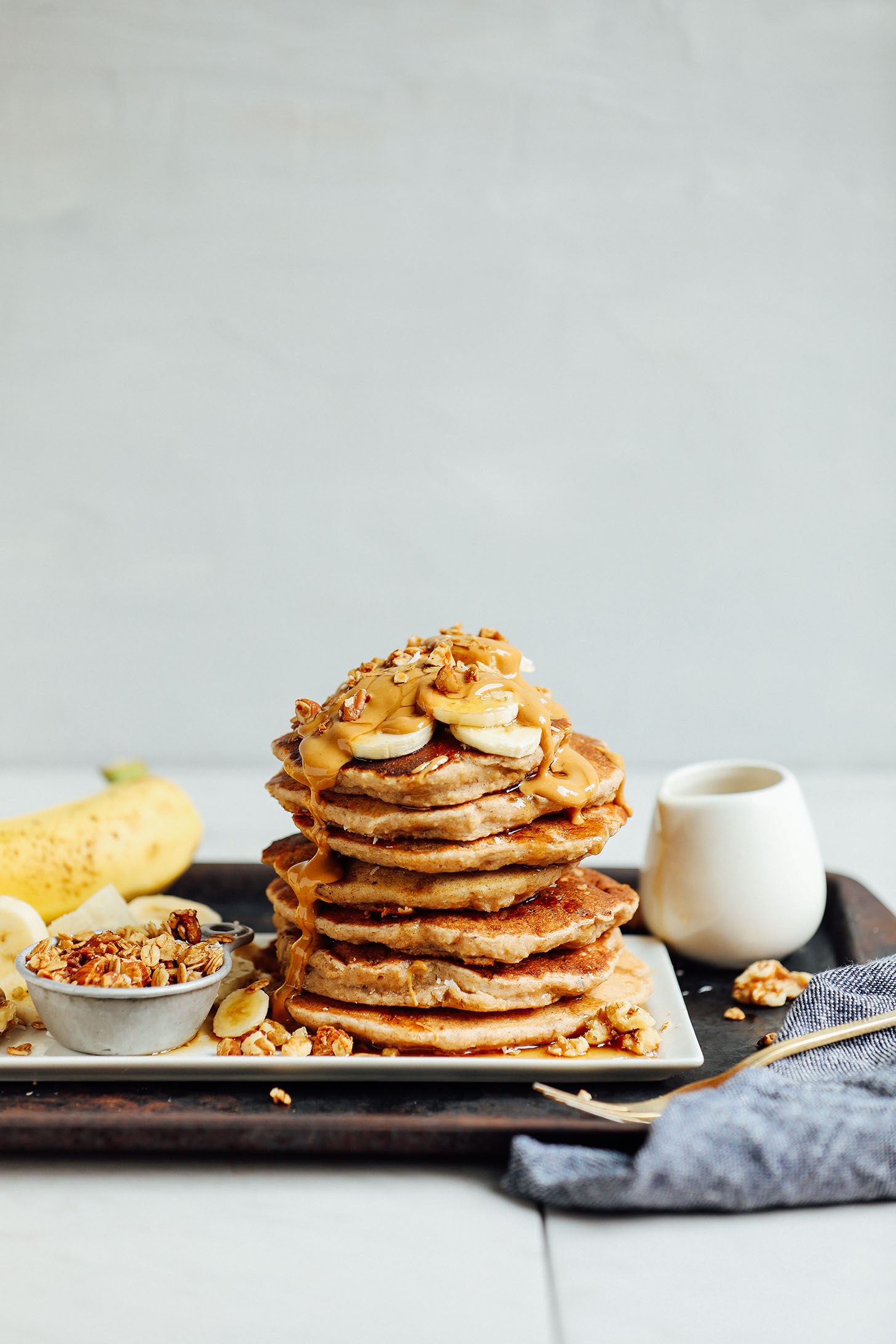 Stack of naturally sweetened gluten-free Banana Pancakes topped with fresh bananas, peanut butter, and walnuts