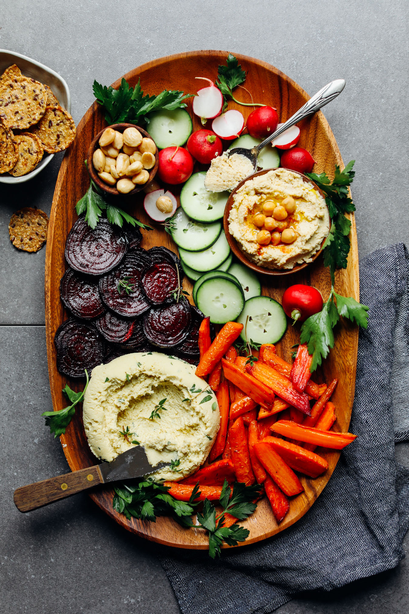 Wood serving platter filled with fresh radishes and cucumbers, roasted beets and carrots, Macadamia Nut Herb Cheese, and hummus