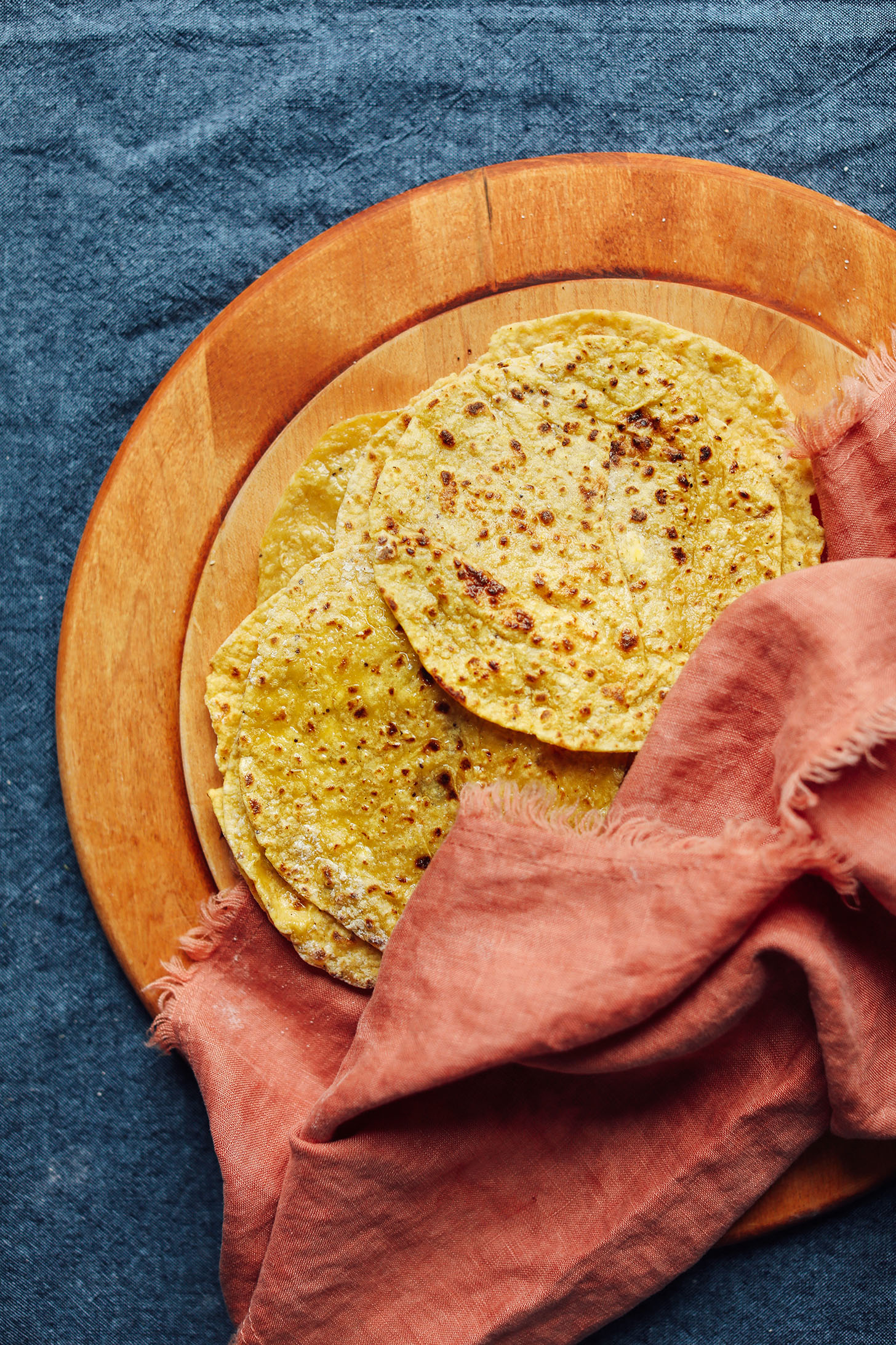 Wood cutting board with homemade 3-Ingredient Plantain Tortillas covered with a towel to keep them warm