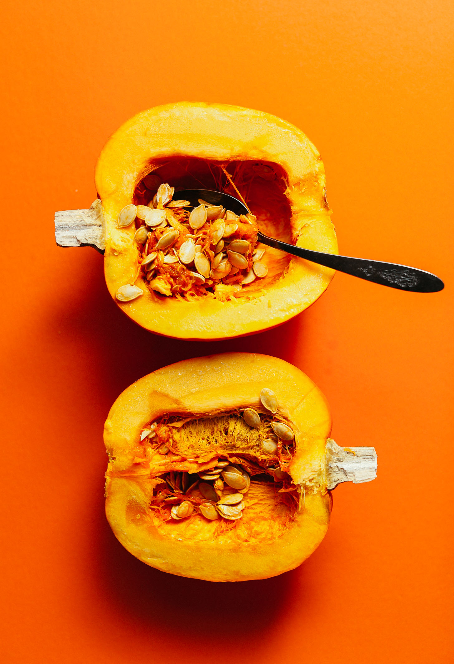 Scooping out the seeds and flesh from a halved pumpkin to make homemade Roasted Pumpkin Seeds