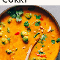 Wooden spoon resting in a pot of vegan pumpkin yellow curry