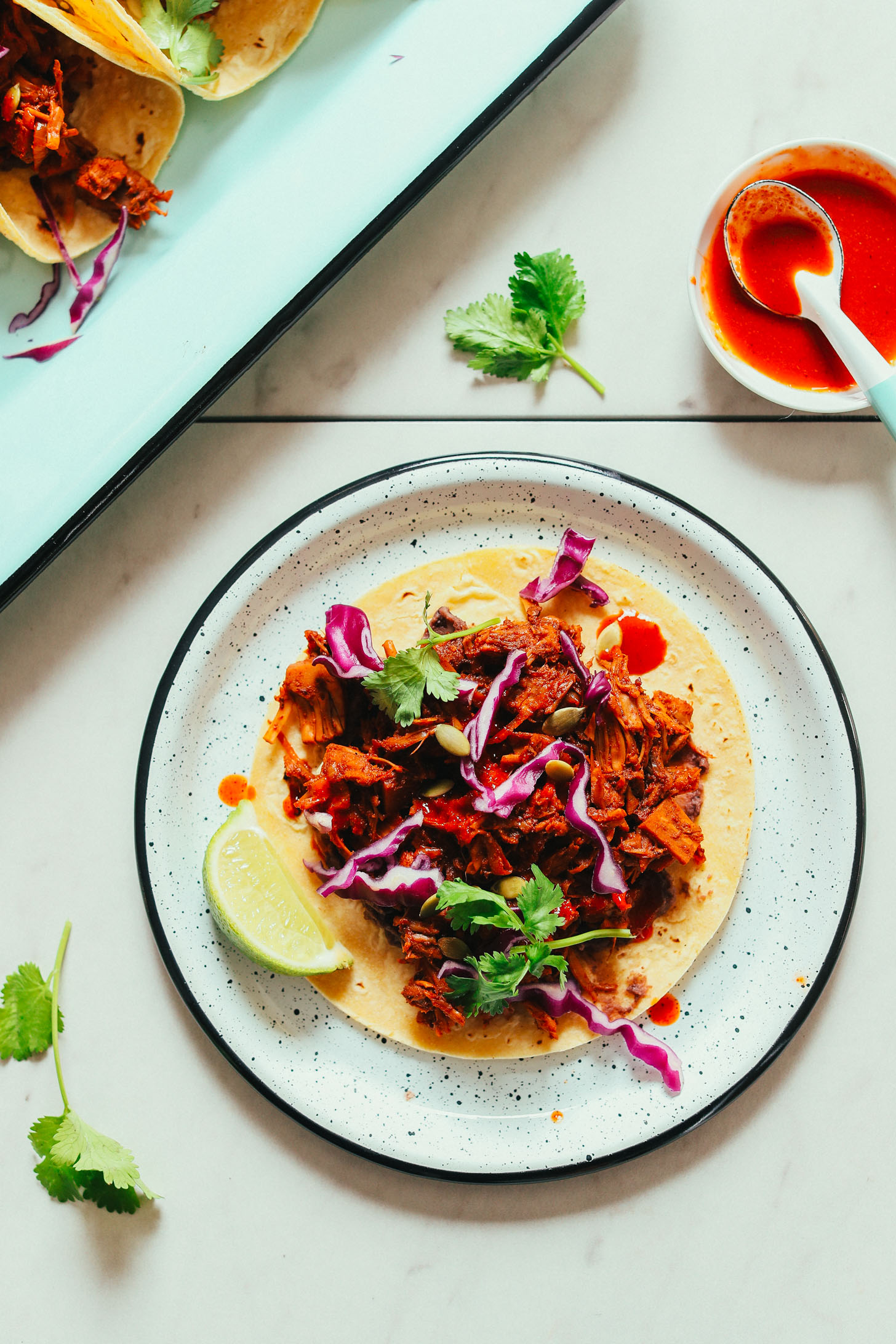 Dinner plate with a corn tortilla topped with jackfruit, cabbage, beans, cilantro, and pumpkin seeds for an amazing plant-based meal