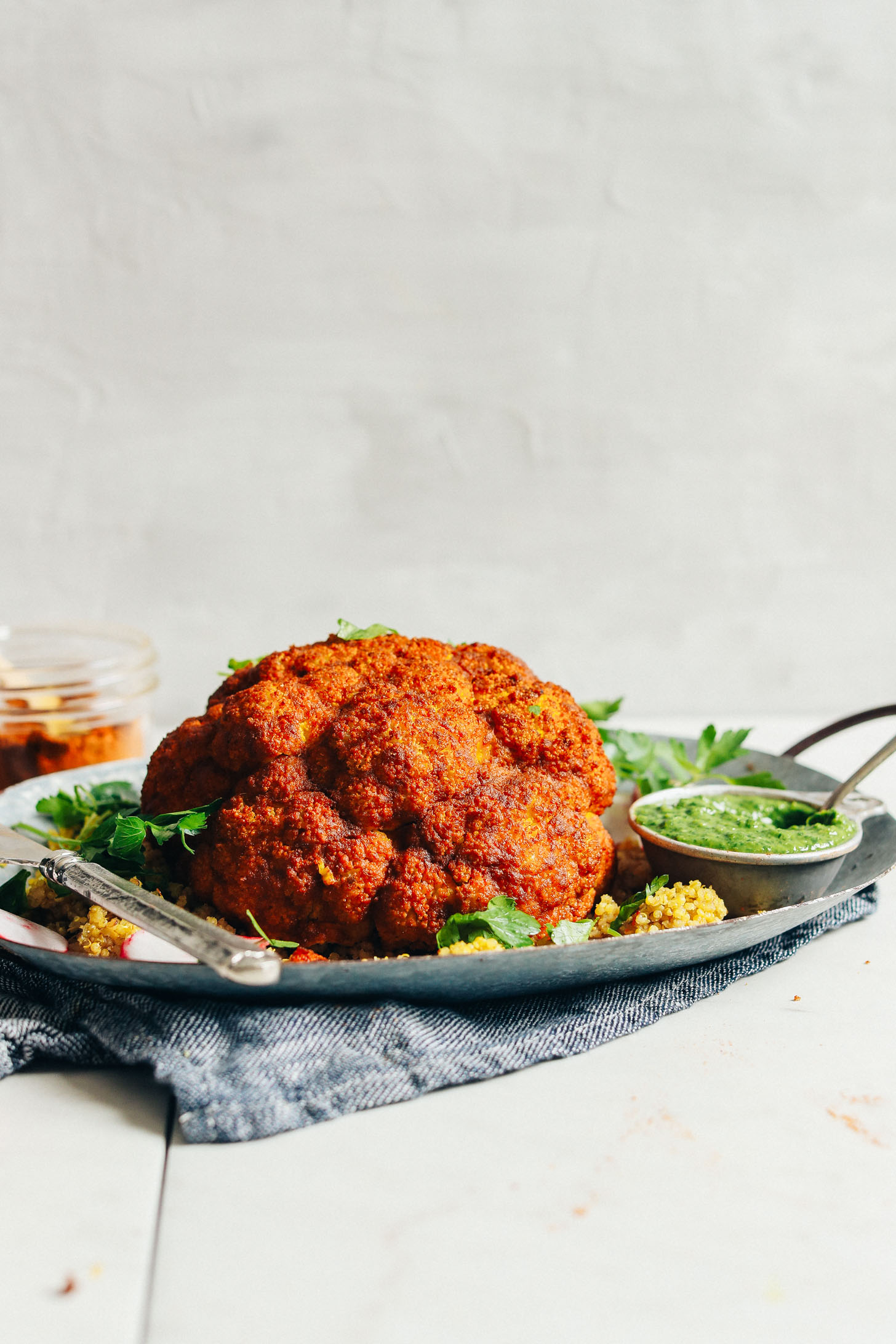 Platter filled with our Whole Roasted Shawarma-Spiced Cauliflower alongside a measuring cup of chimichurri