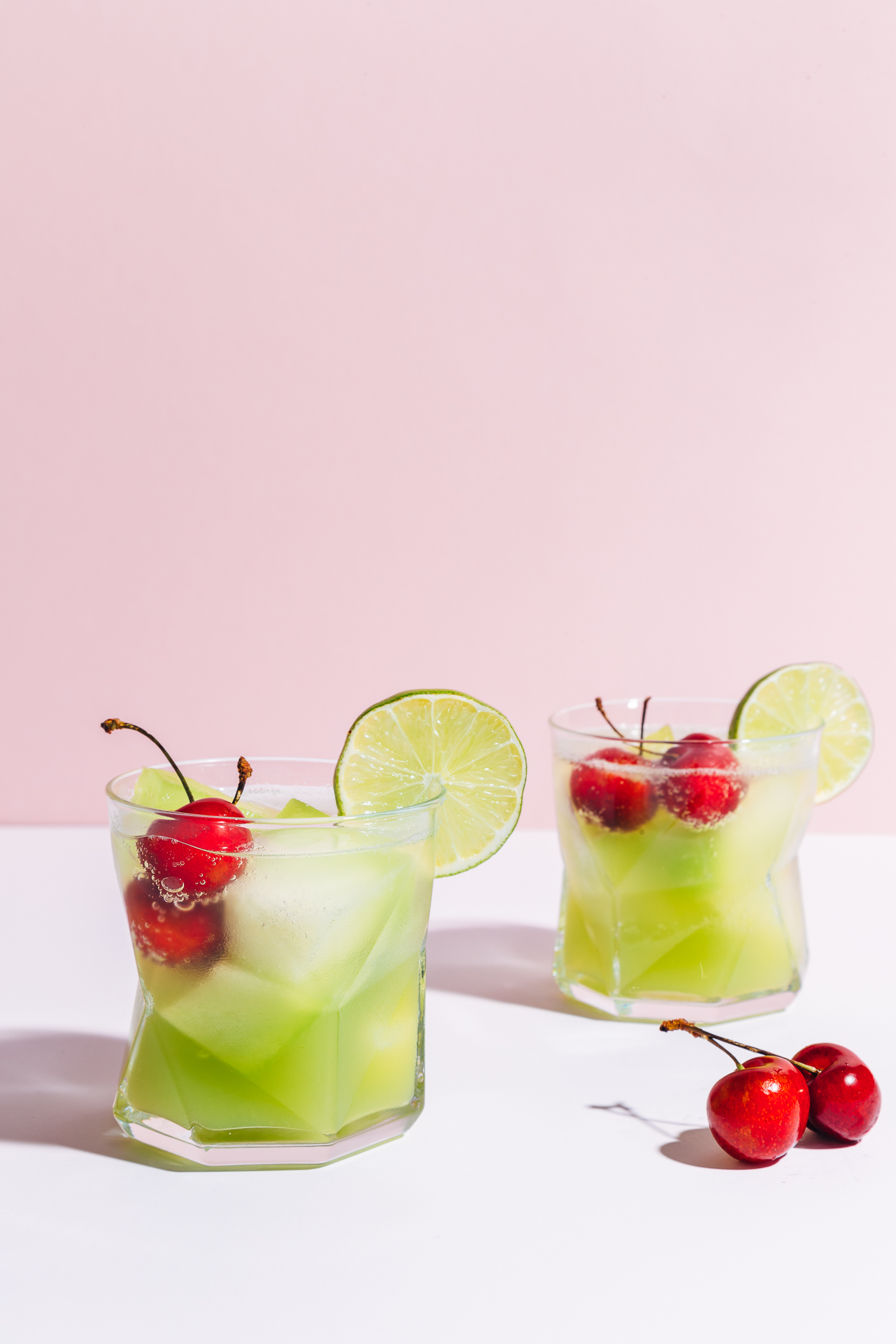 Two glasses of our Citrus & Melon Spritzer with fresh cherries in the glasses