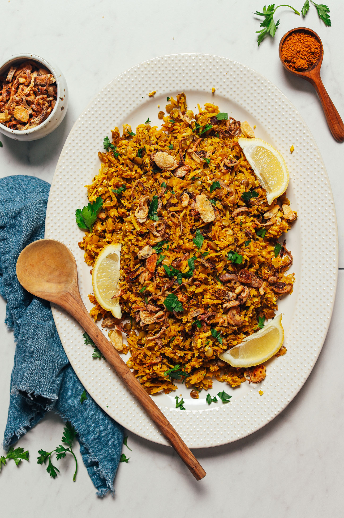Wooden spoon resting on a platter of Grain-Free Mujadara beside crispy shallots and curry powder