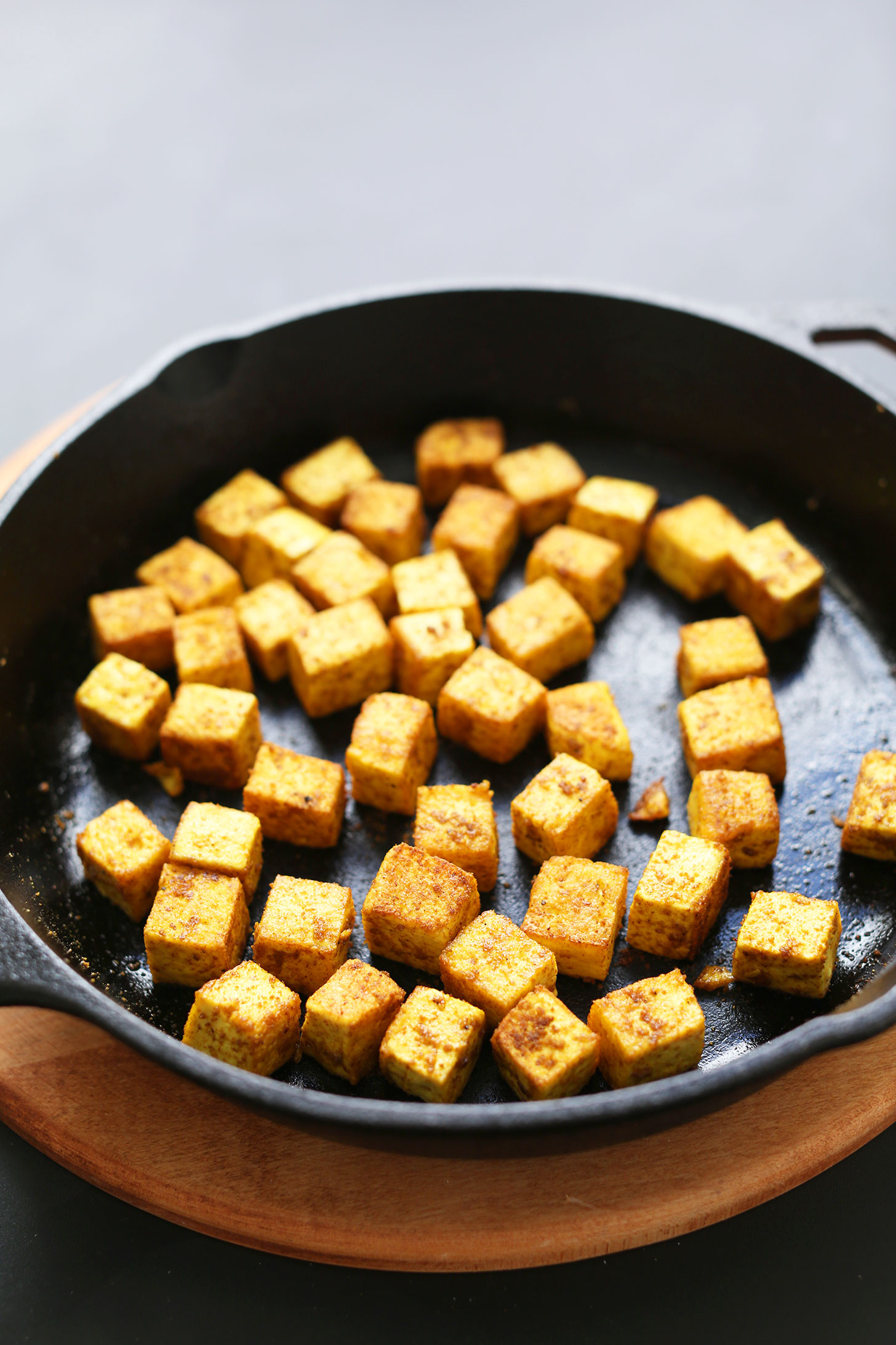 Tofu being sautéed with curry powder in a cast iron skillet