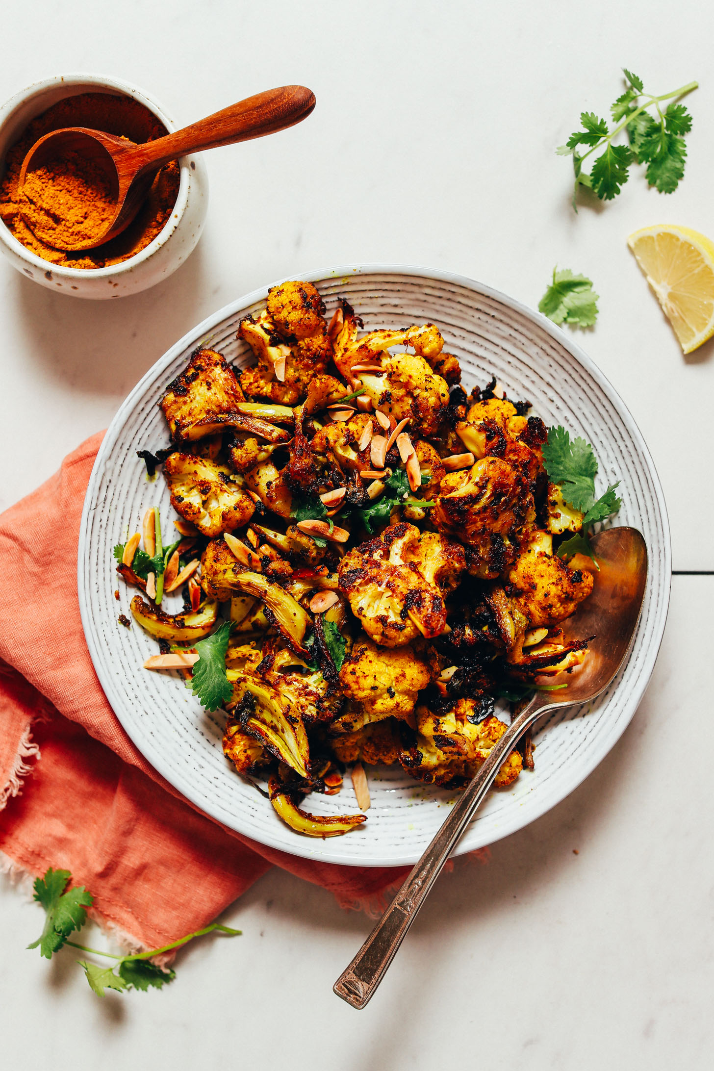 Curry powder, lemon slice, and cilantro beside a bowl of Quick Crispy Cauliflower