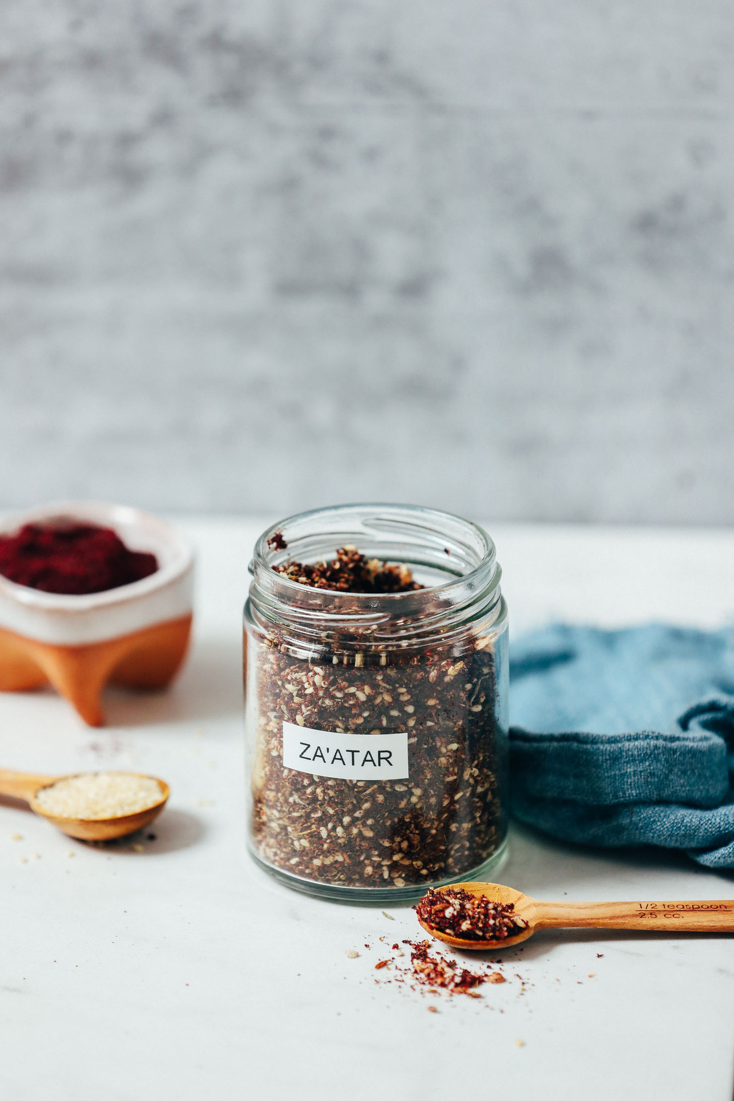 Spoonful and jar of za'atar seasoning next to sesame seeds and sumac