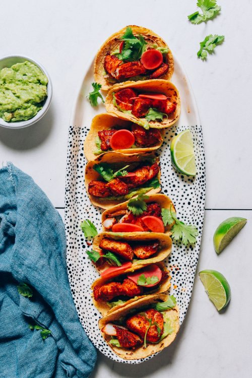 Platter filled with Spicy Baked Fish Tacos beside guacamole and lime wedges