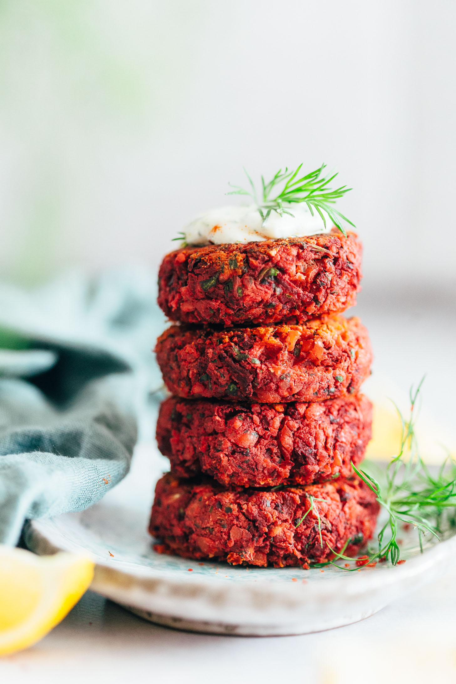 Lemon wedge next to a plate of stacked Beet Falafel and fresh dill