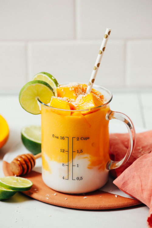 Measuring glass of our mango lassi smoothie topped with frozen mango chunks and sliced lime