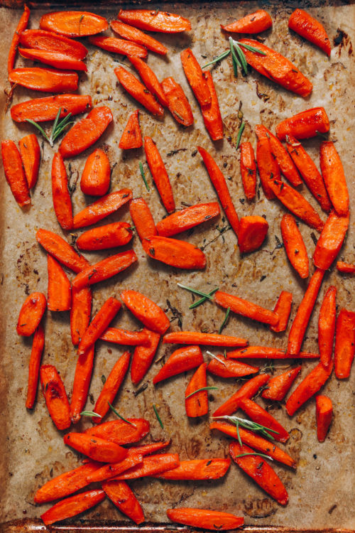 Parchment-lined baking sheet of perfect roasted carrots with fresh herbs