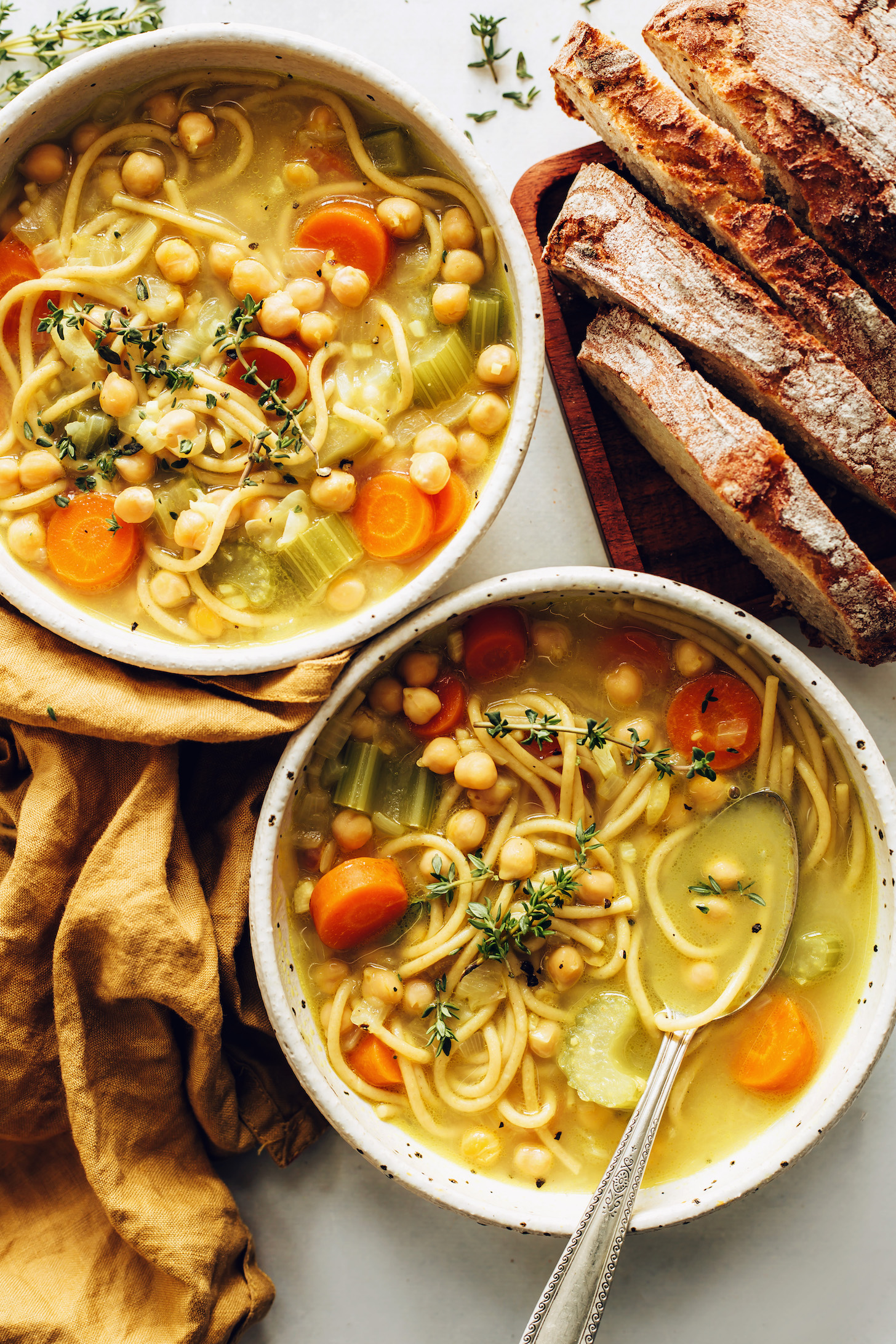 Sliced sourdough bread next to two bowls of chickpea noodle soup