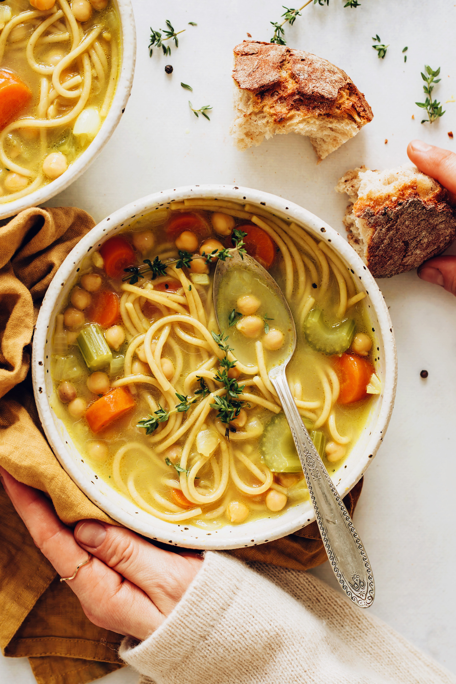 Sourdough bread beside a bowl of chickpea noodle soup topped with fresh thyme