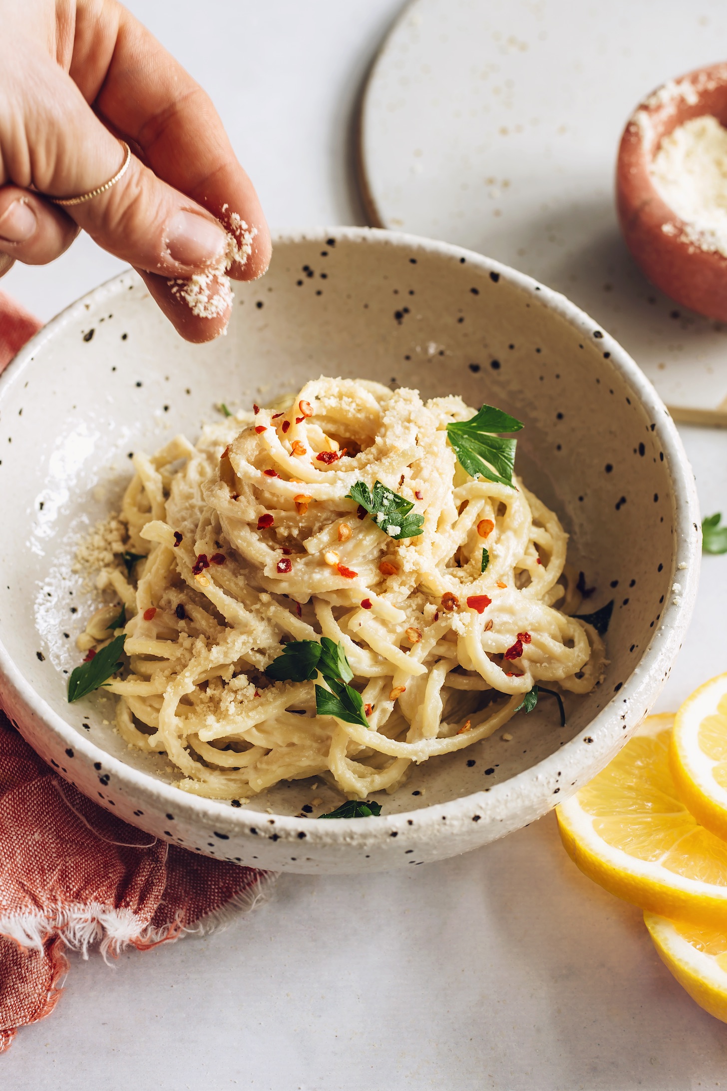 Sprinkling vegan parmesan cheese over a bowl of pasta al limone