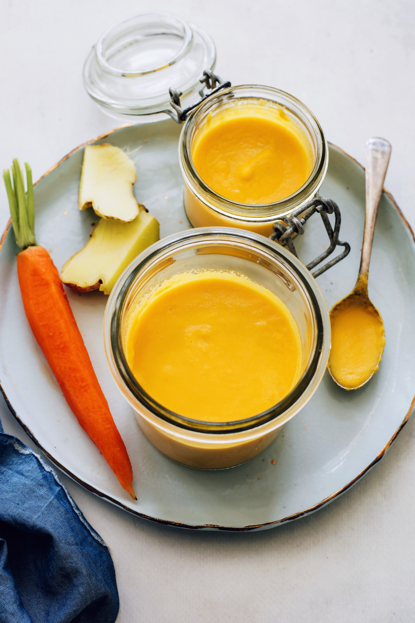 Jars and spoonful of carrot ginger dressing next to a carrot and fresh ginger