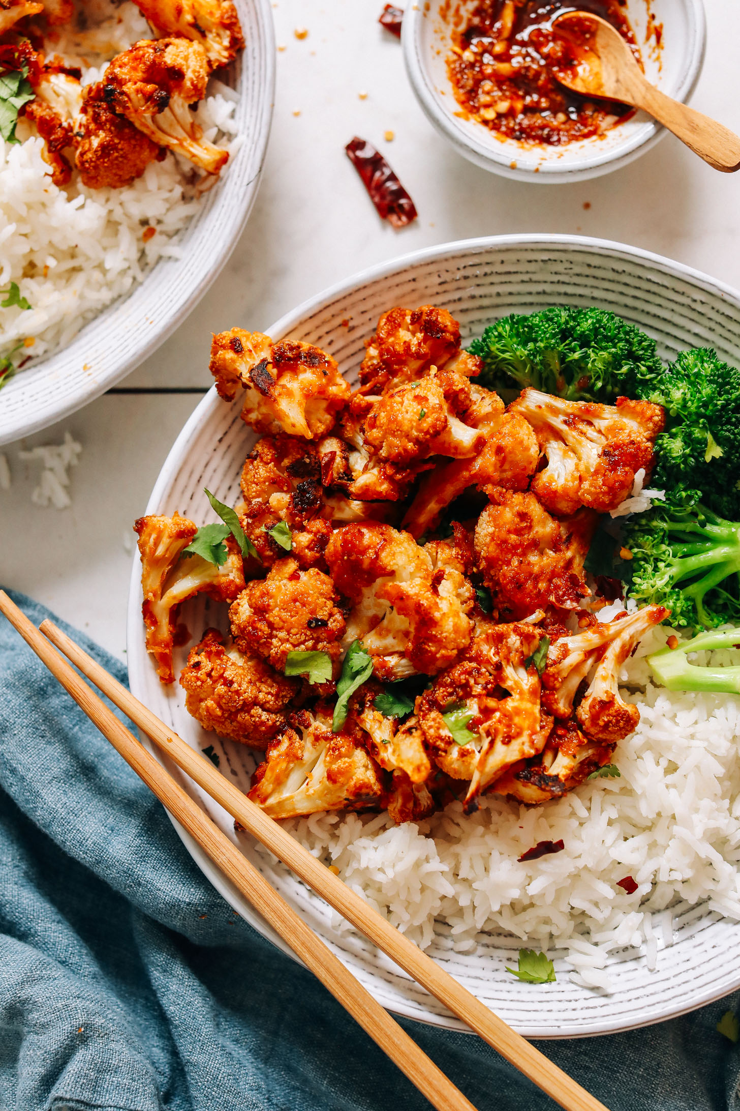 Chopsticks resting on a bowl of General Tso's Cauliflower with grains and veggies