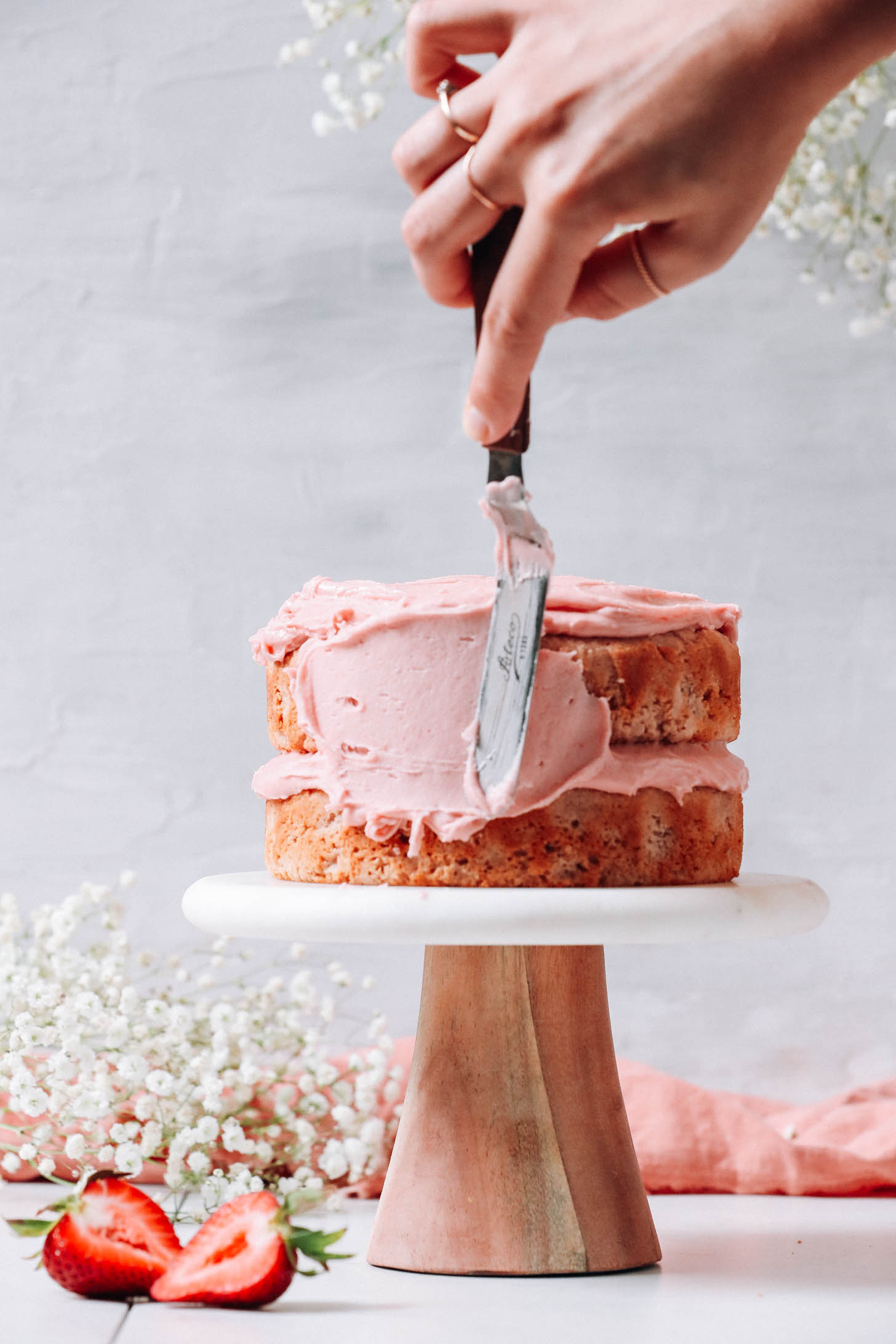 Spreading strawberry frosting on strawberry cake