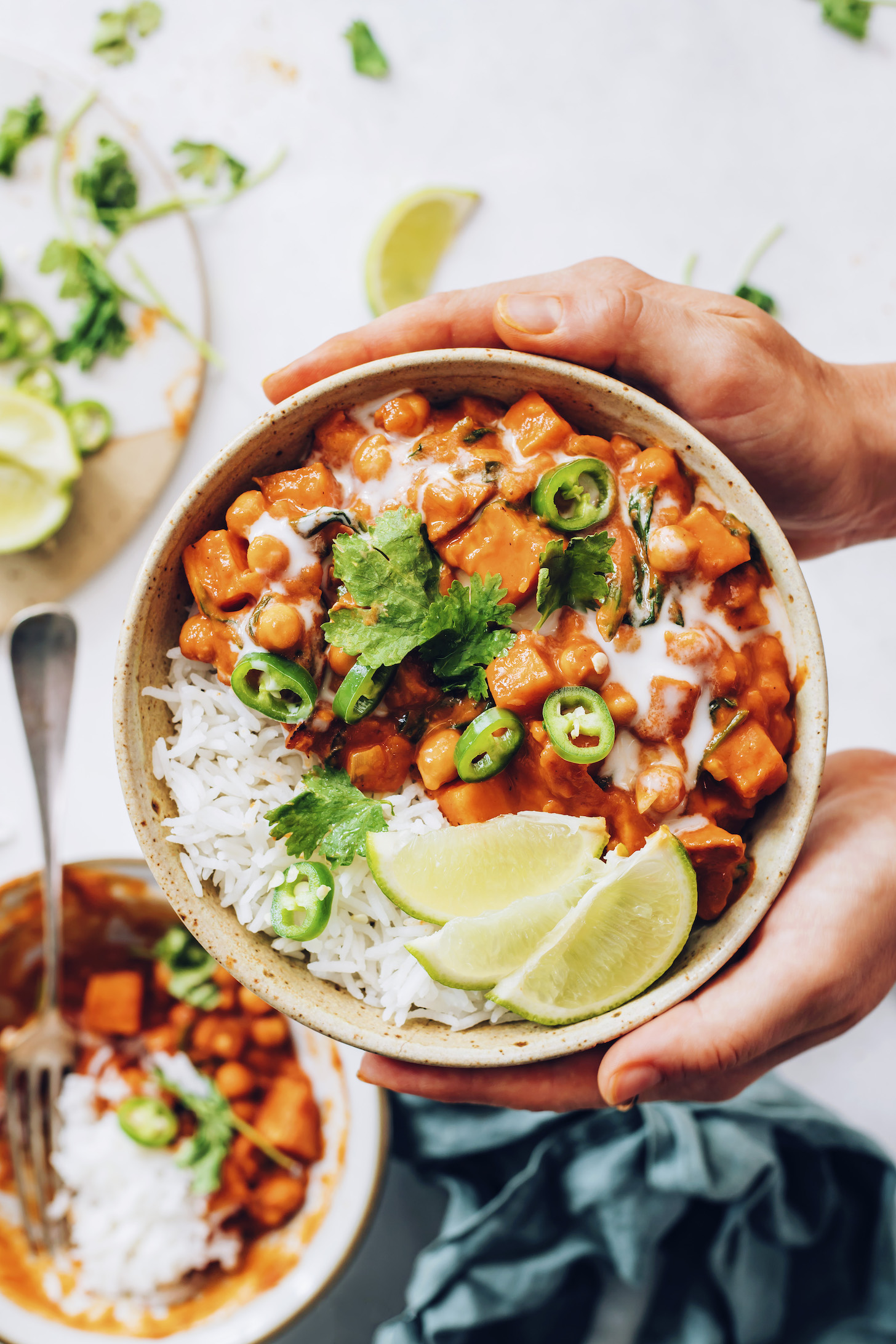 Holding a bowl of roasted red pepper chickpea curry served with white rice, limes, jalapeño, and cilantro