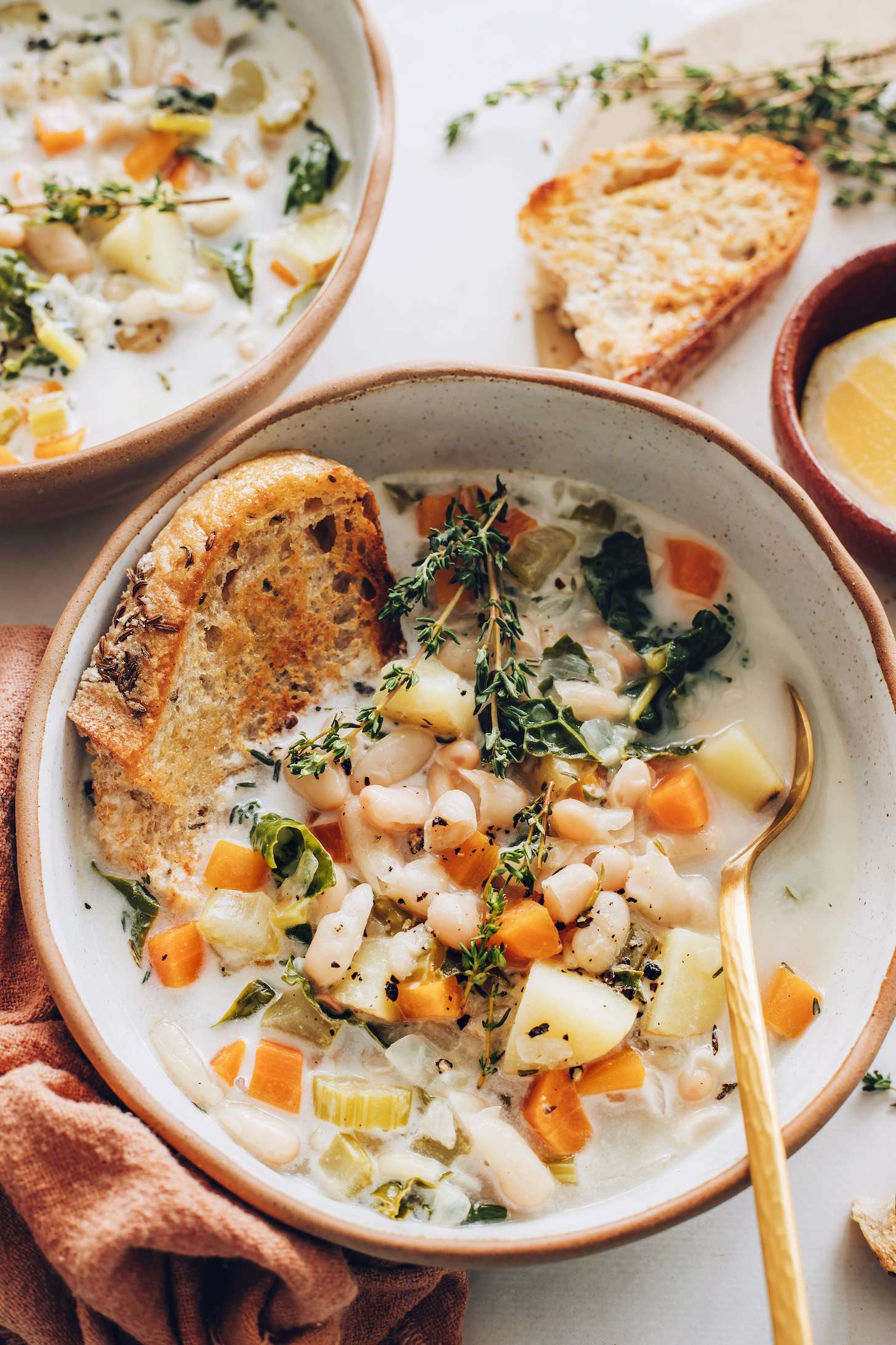 Slices of toasted bread in and beside bowls of vegan white bean soup