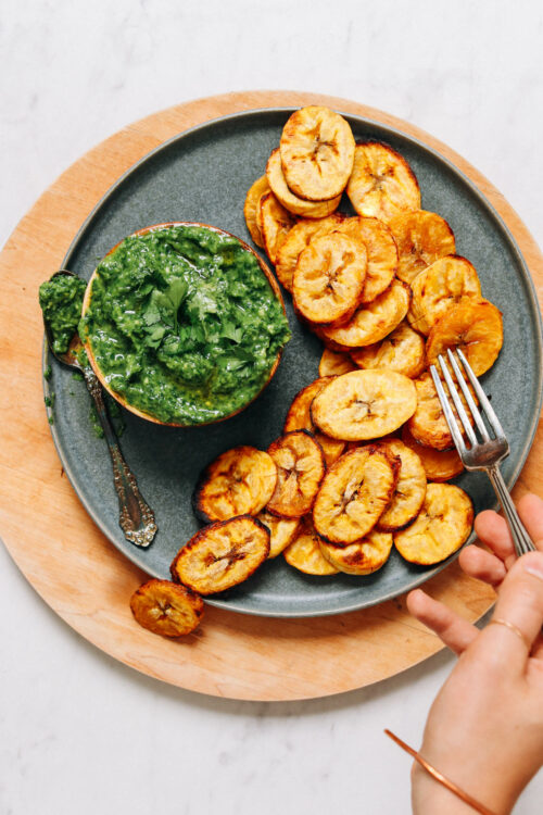 Plate of roasted plantains with a bowl of magic green sauce