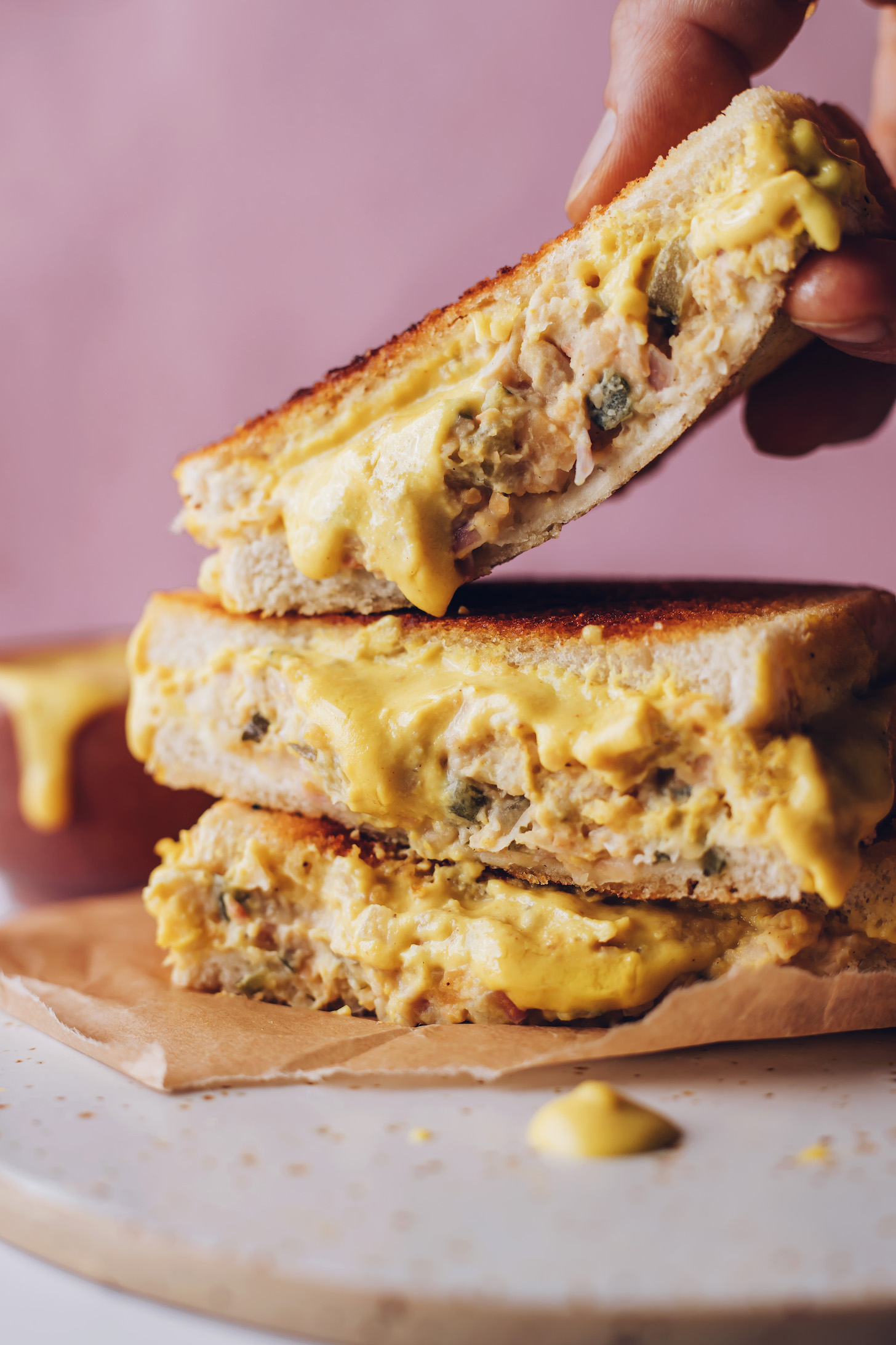 Picking up a vegan tuna melt from a stack of sandwiches
