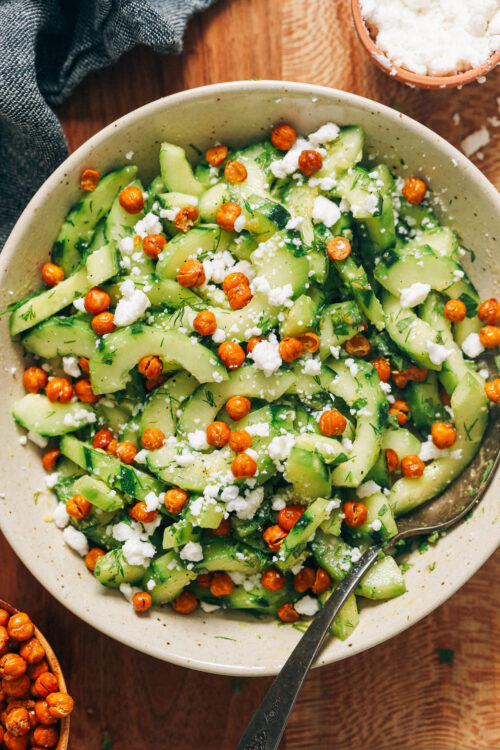 Bowl of cucumber salad with fresh dill and mint and topped with crispy chickpeas and vegan feta