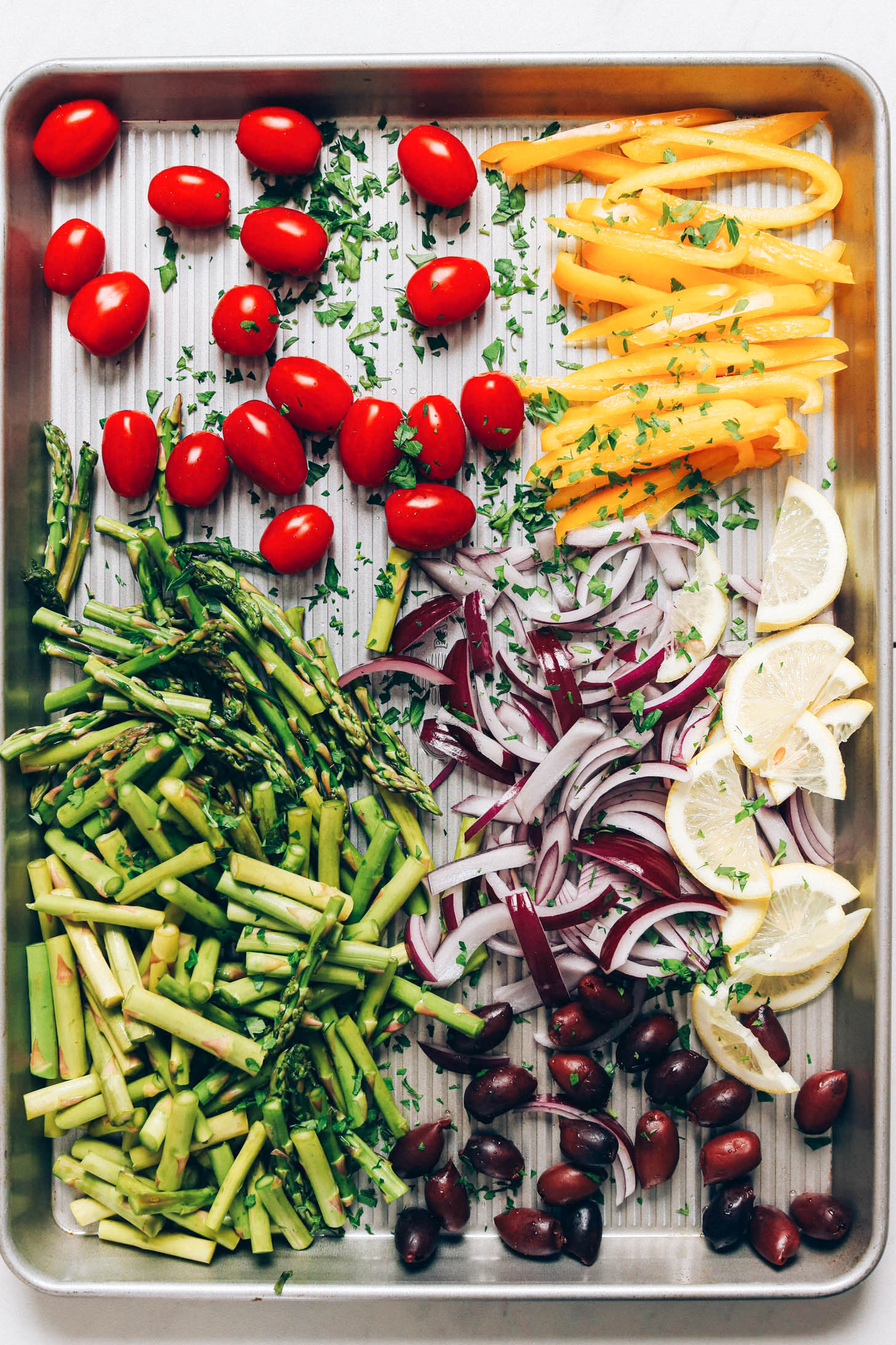 Chopped vegetables, lemon, and olives on a baking sheet