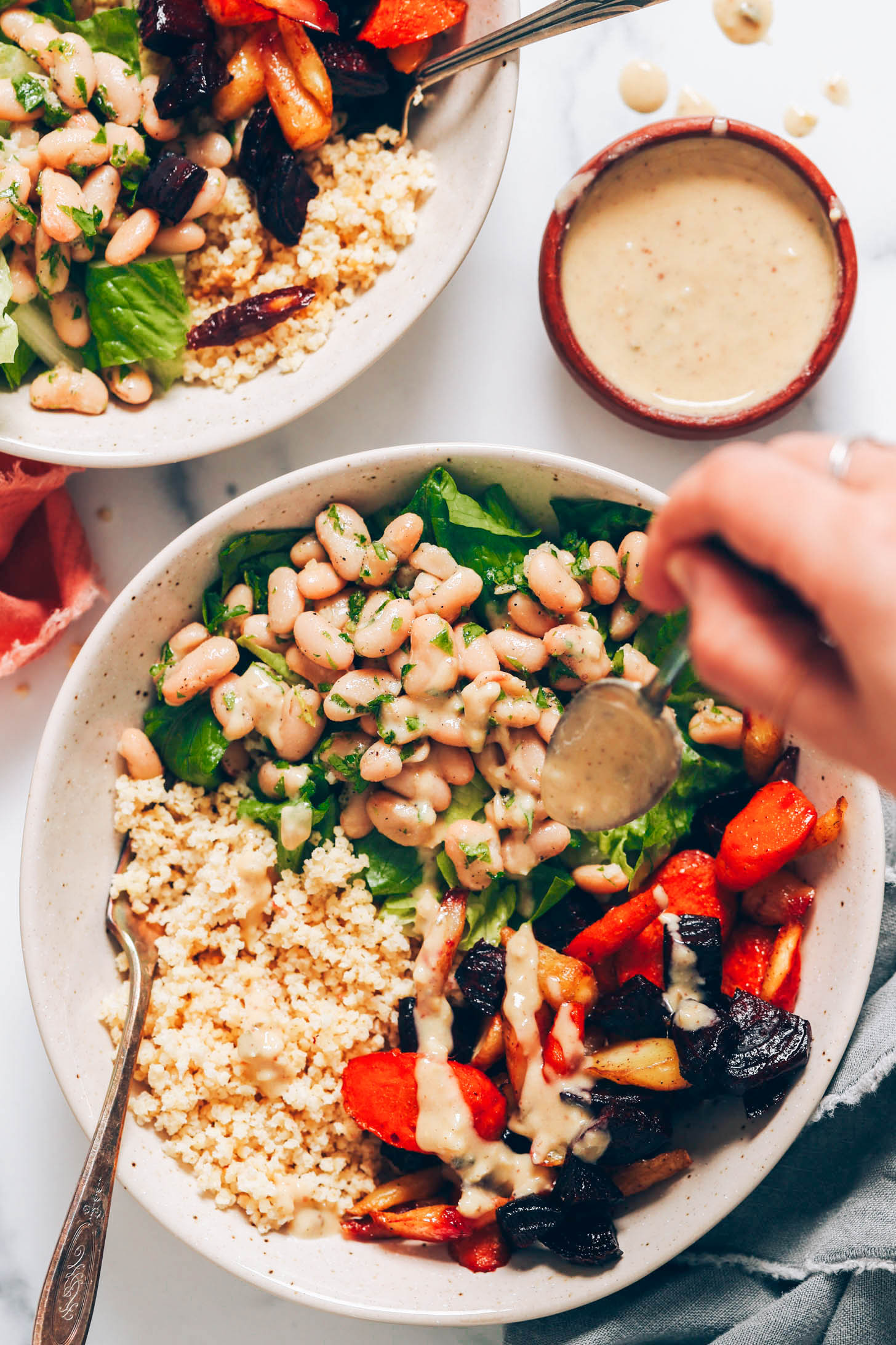 Drizzling hummus caesar dressing onto roasted veggies, grains, lettuce, and white beans