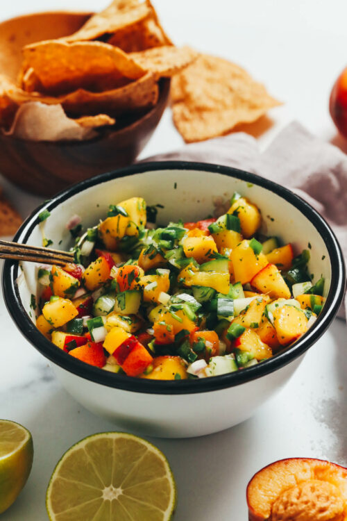 Tortilla chips next to a bowl of fresh peach cucumber salsa