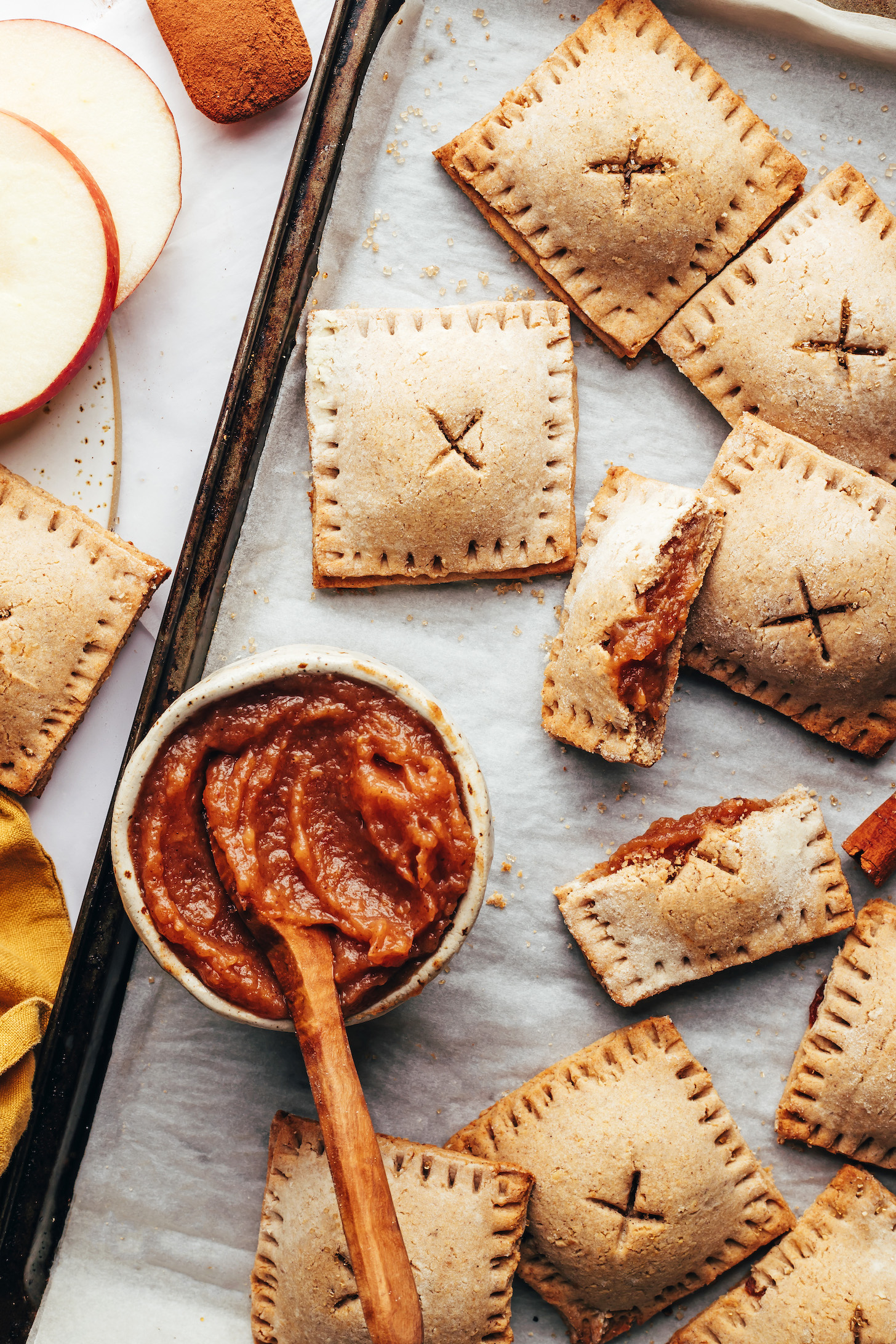 Mini apple butter pop tarts on a baking sheet next to a bowl of apple butter