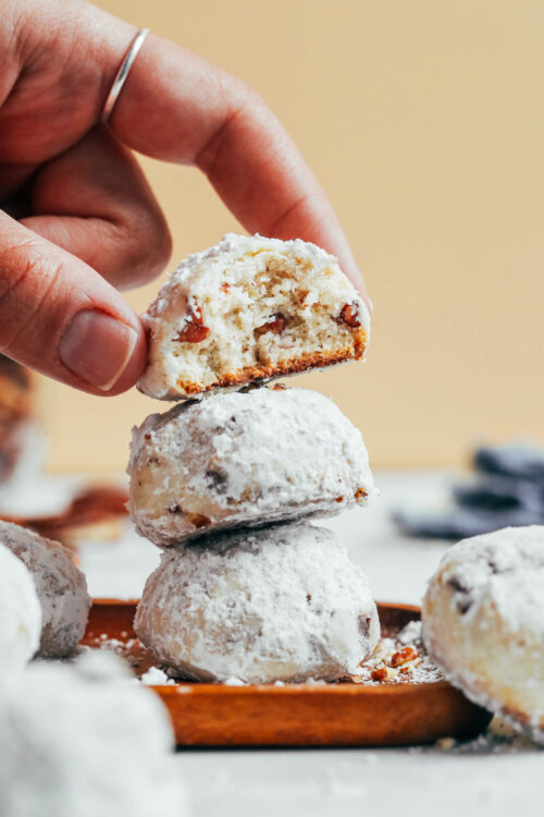 Reaching in to place a vegan gluten-free Mexican wedding cookie on a stack of two cookies