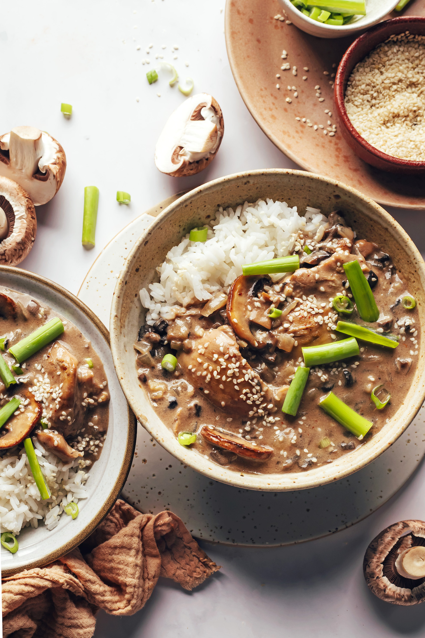 Two bowls of Samoan-inspired mushroom chicken with rice, green onions, and sesame seeds