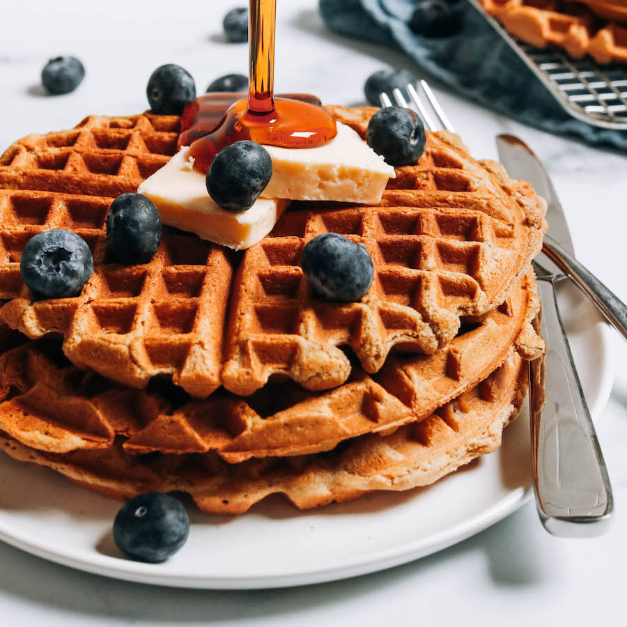 Drizzling maple syrup onto a stack of protein waffles