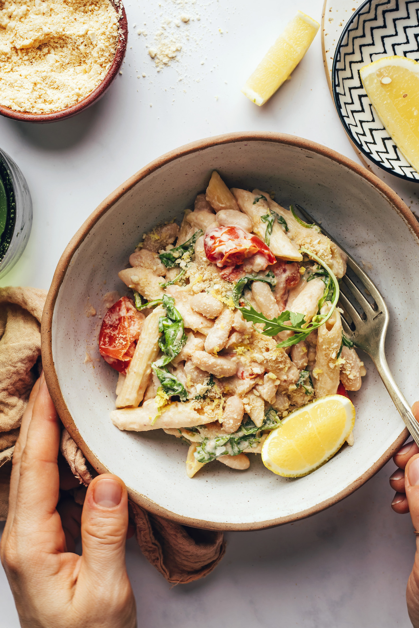 Hand holding a bowl and fork in a bowl of lemon garlic pasta with veggies