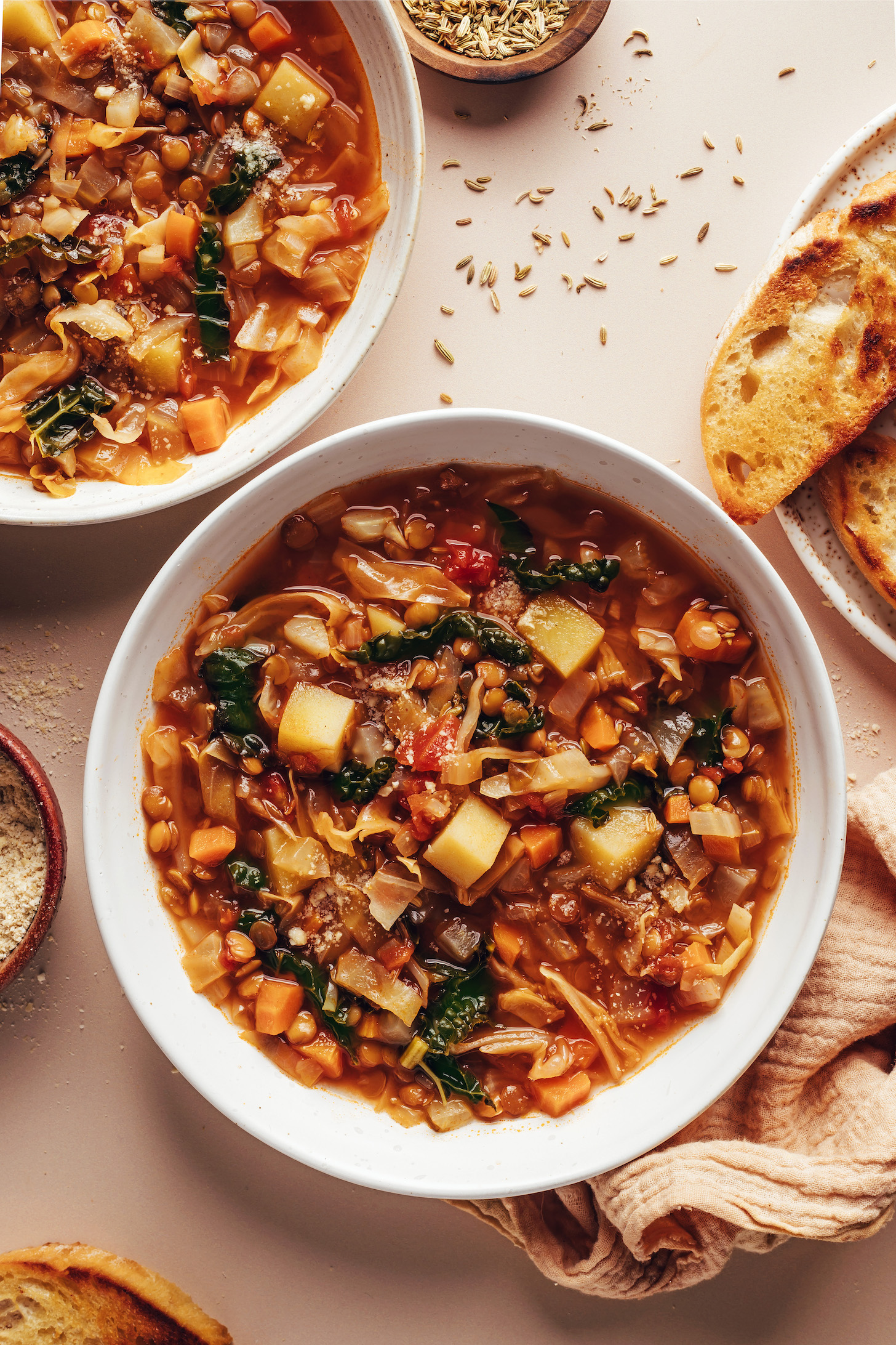 Two bowls of cabbage, fennel, and lentil soup next to fennel seeds and toasted bread