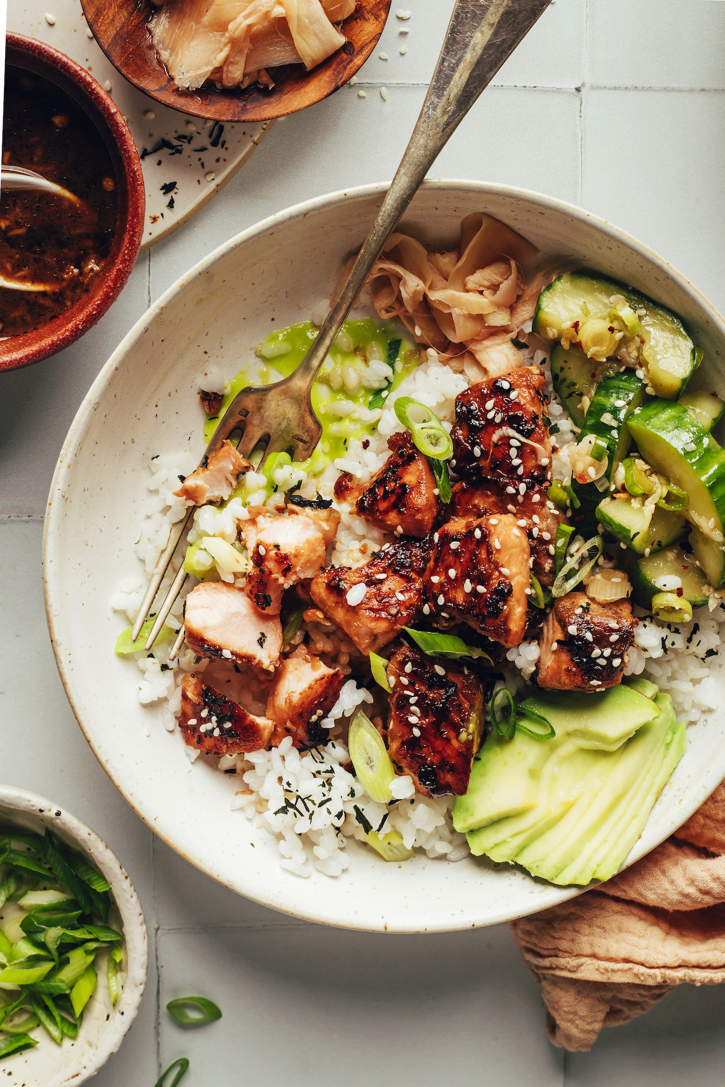 Salmon sushi bowl with tamari-glazed salmon, avocado, green onion, seaweed, cucumber salad, pickled ginger, and rice