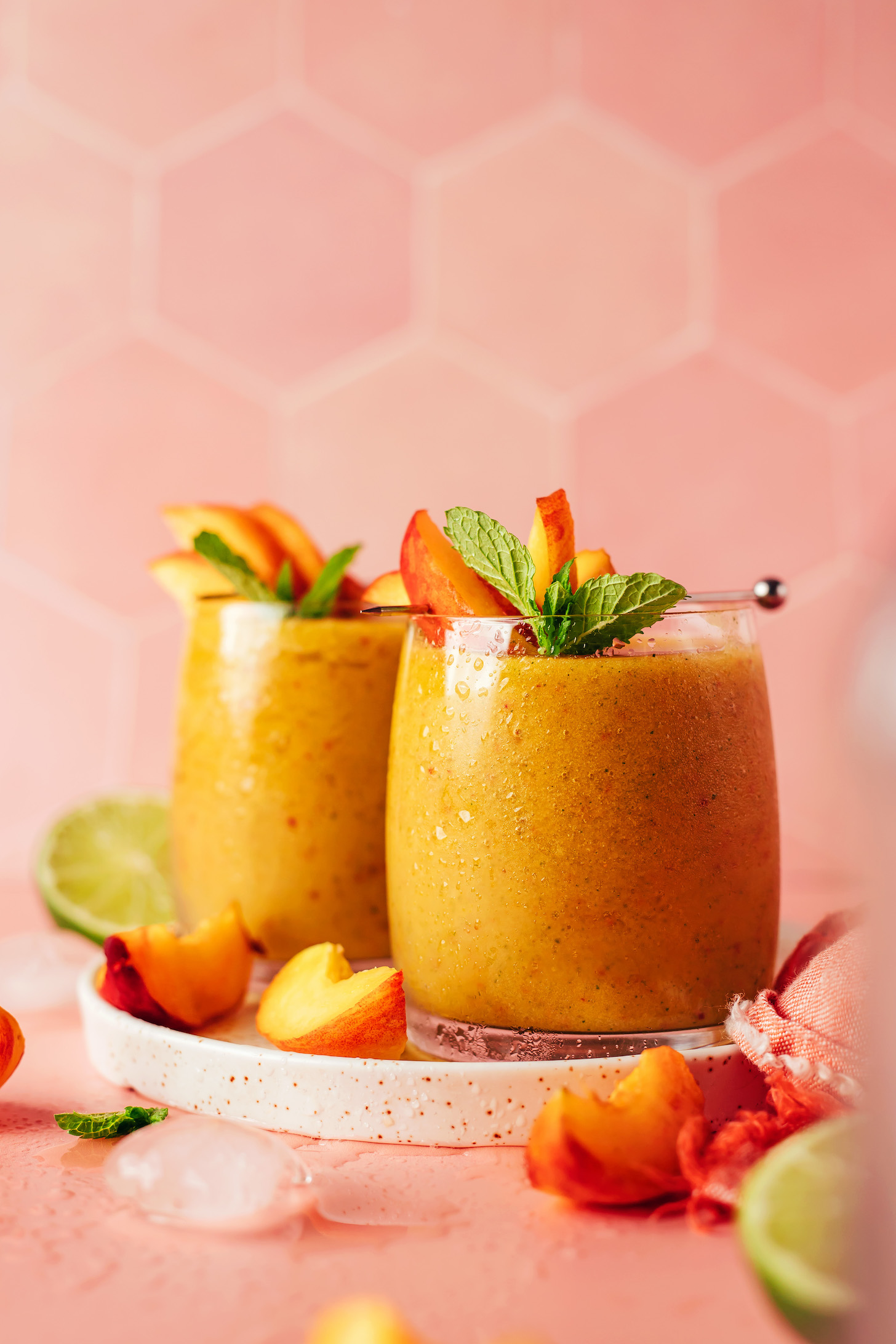 Two glasses of our frozen peach daiquiri on a plate with peach slices