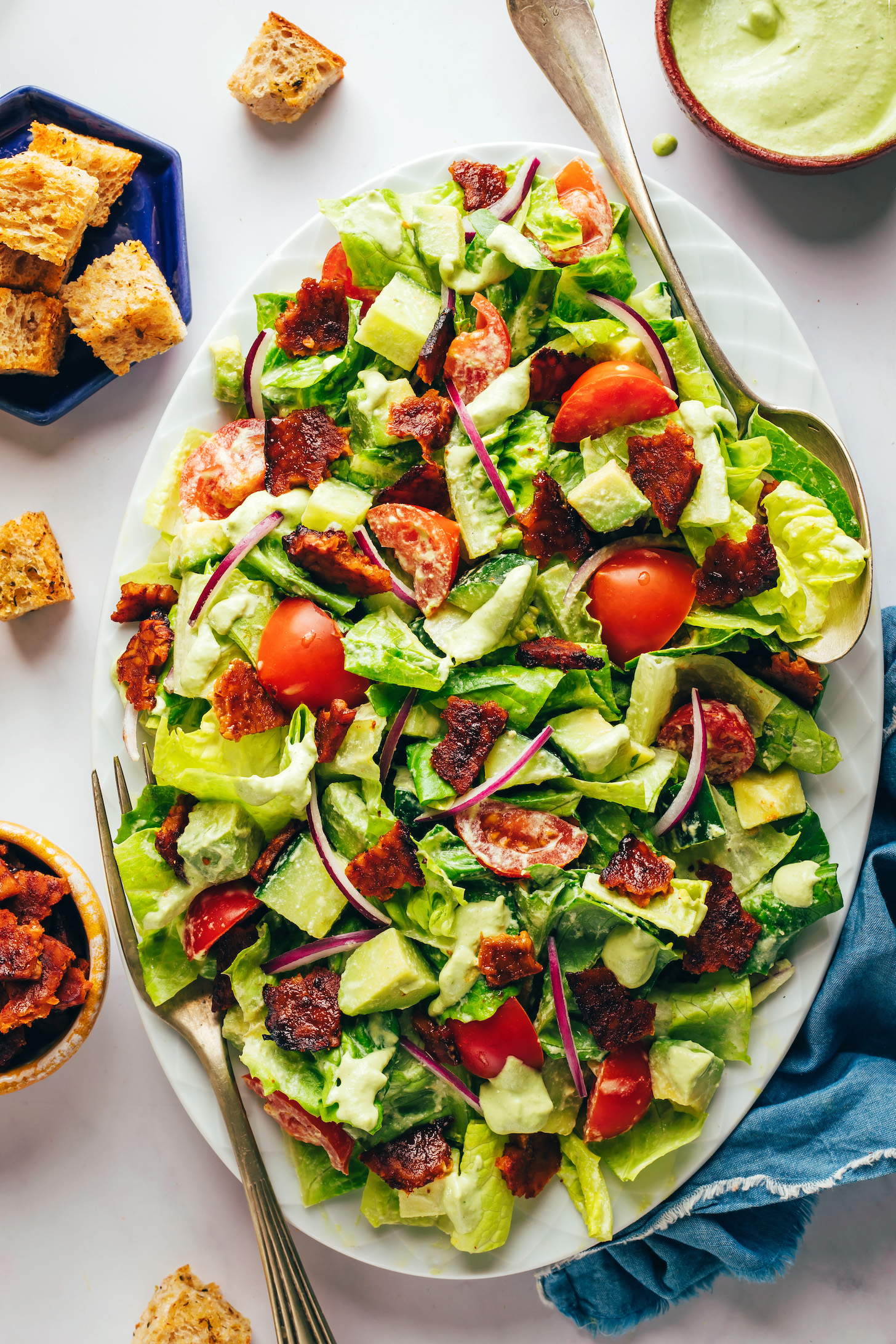 Overhead shot of a platter of our vegan blt salad with ranch dressing, croutons, and tempeh bacon next to it