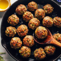 Spoon holding a turkey meatball in a cast iron skillet of more meatballs